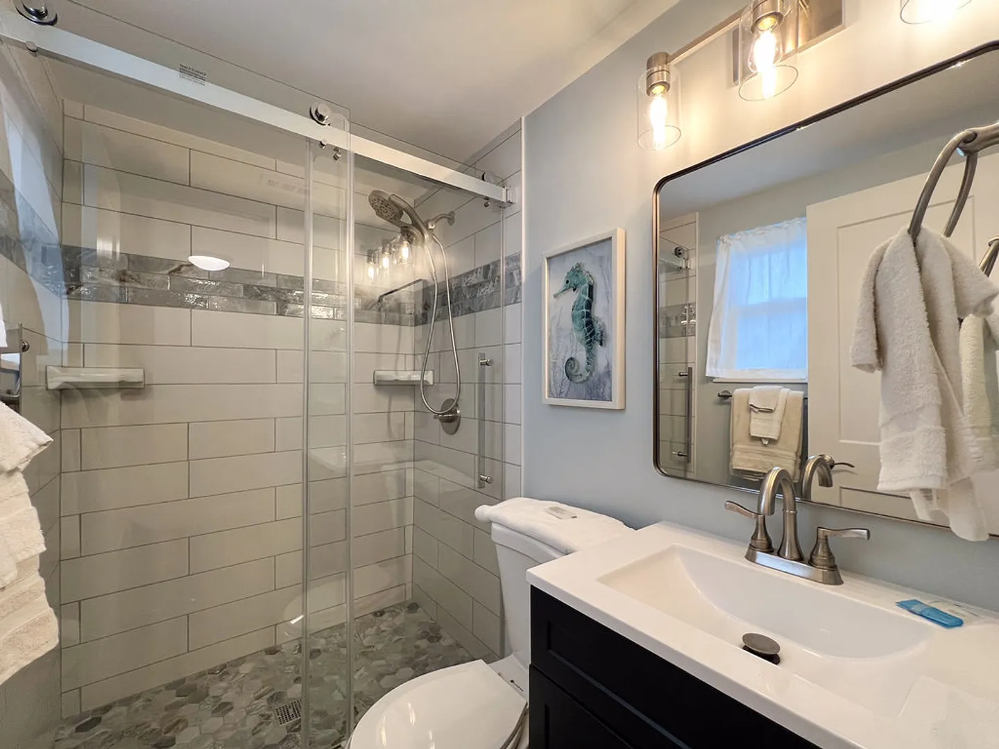 Bathroom with a glass-enclosed walk-in shower, toilet, and vanity sink with a framed mirror.