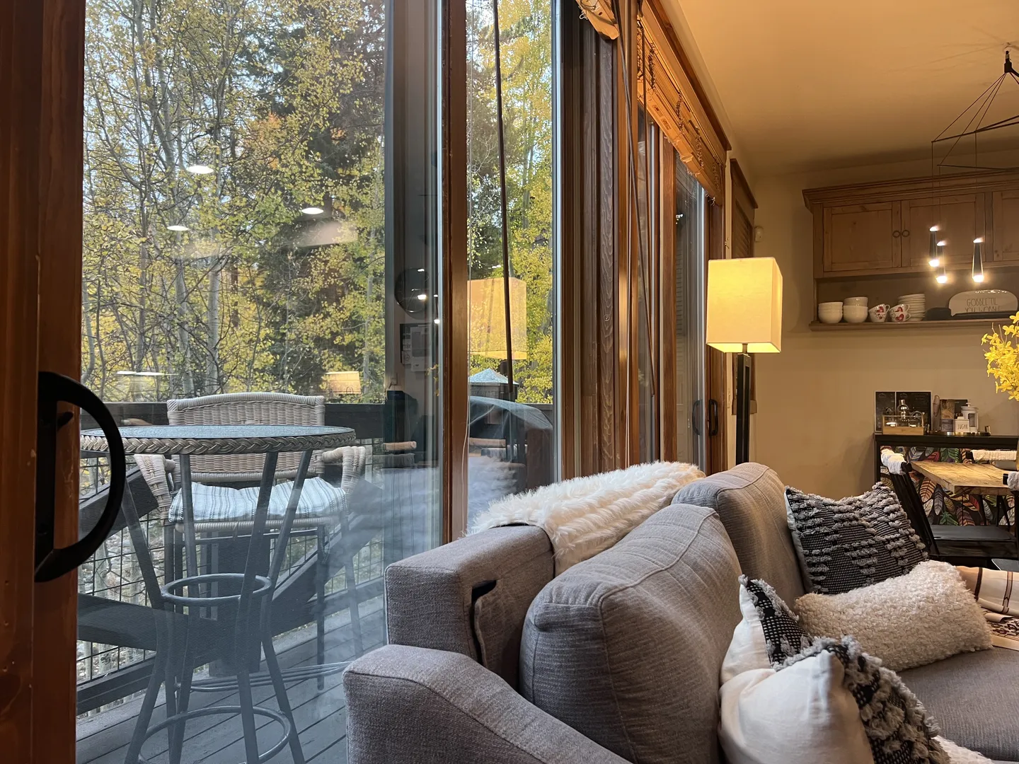 A living room sofa positioned next to sliding glass doors looking out onto an outdoor deck surrounded by trees.