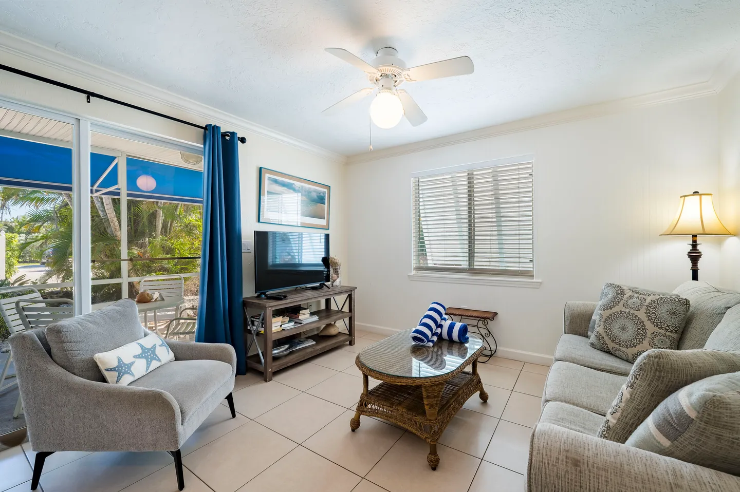 Living room with tiled floor, sofa, armchair, coffee table, TV console, ceiling fan, and sliding glass door leading to a patio.