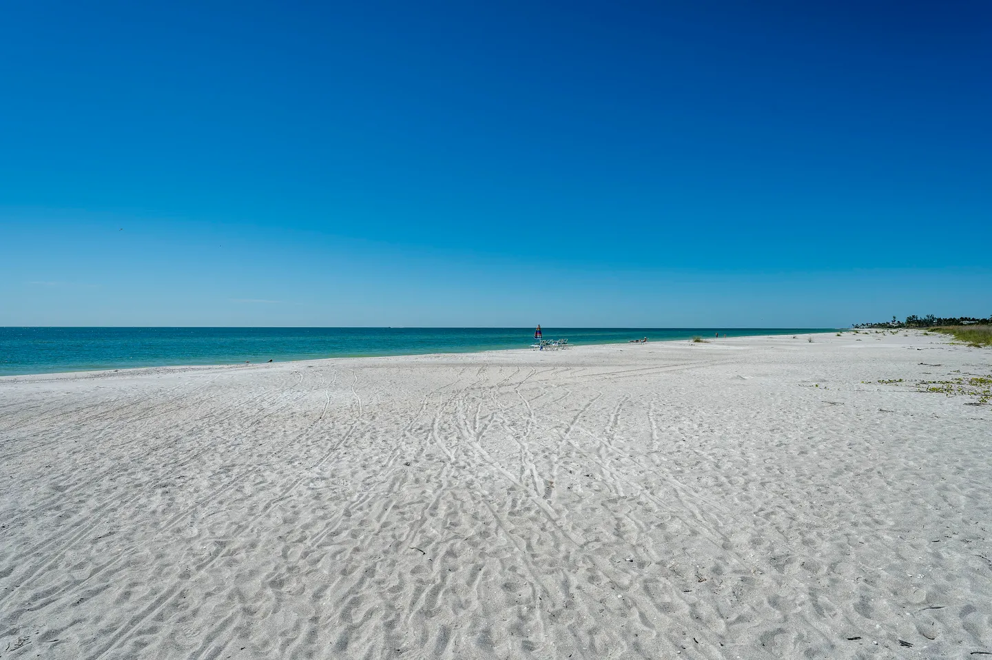 Wide view of a white sand beach meeting the turquoise ocean under a clear blue sky.