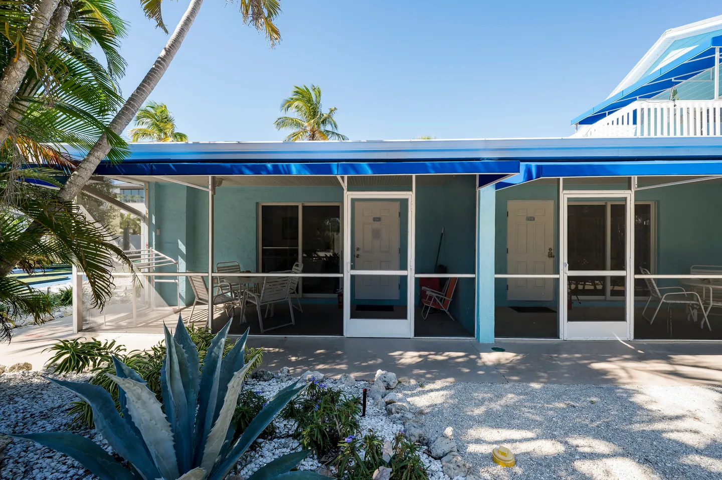 Exterior view of screened porches with patio furniture outside light blue vacation units under a bright blue sky.
