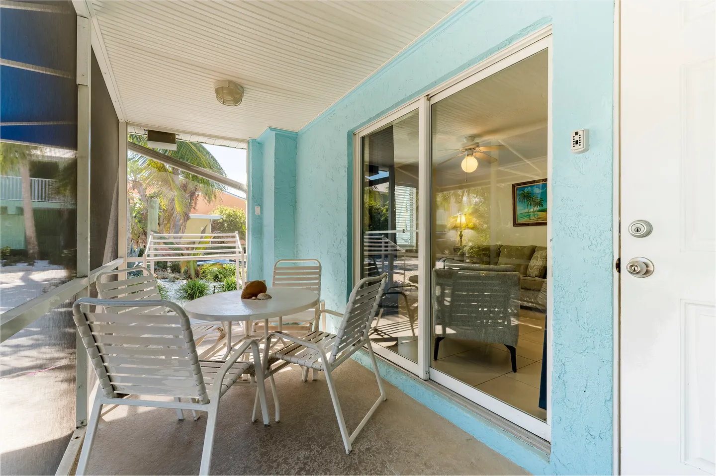 Screened porch with outdoor table, chairs, light blue stucco wall, and sliding glass doors looking inside.