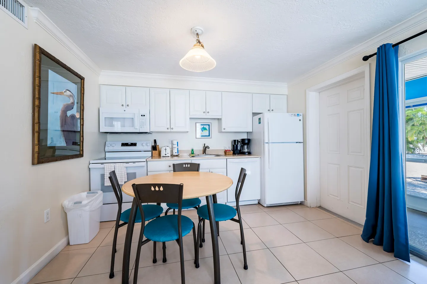 Kitchen and dining area featuring a round table with blue chairs, white appliances, and white cabinetry.