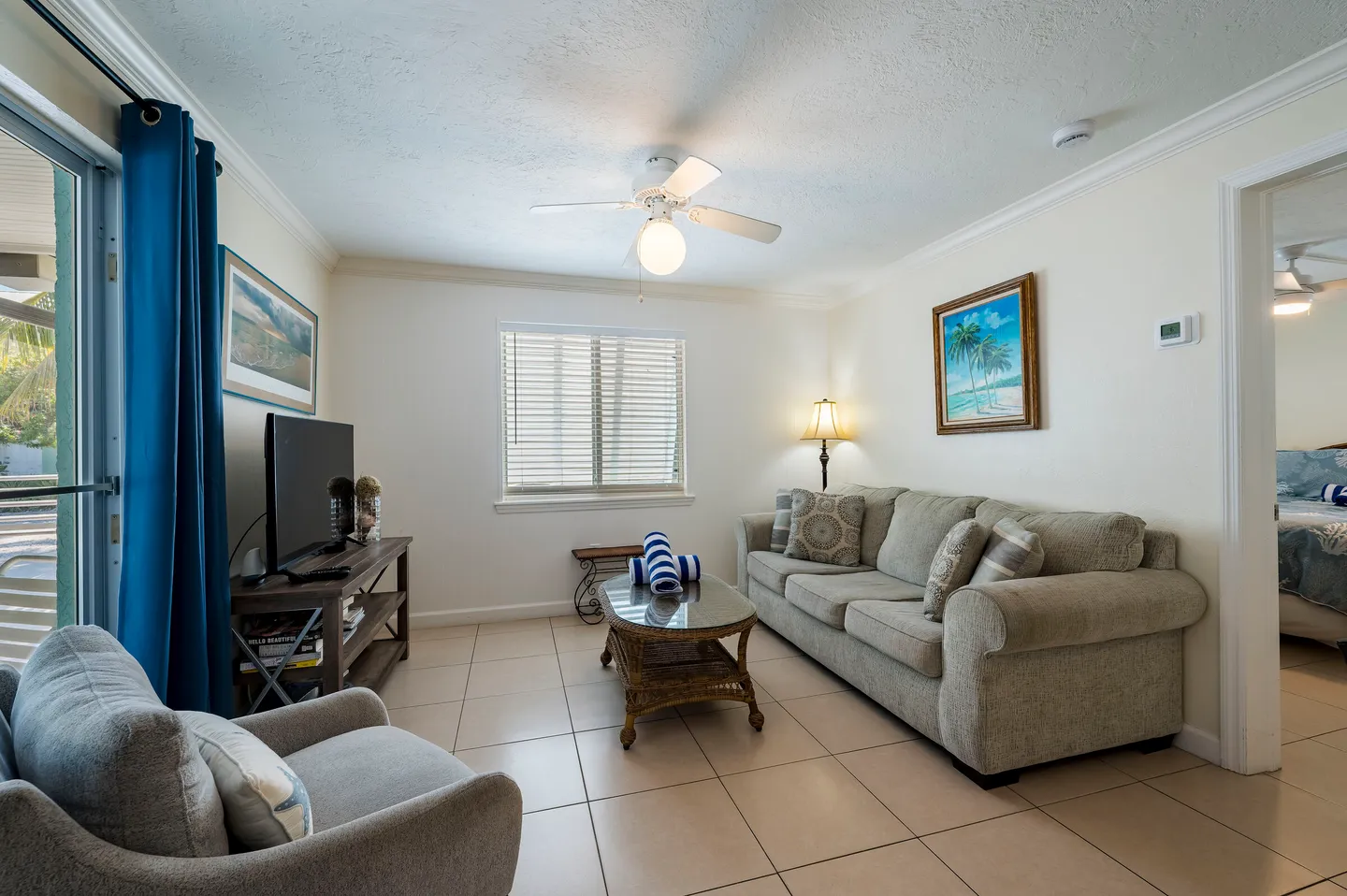 Living room with a sofa, armchair, coffee table, TV stand, tiled flooring, and sliding glass door.