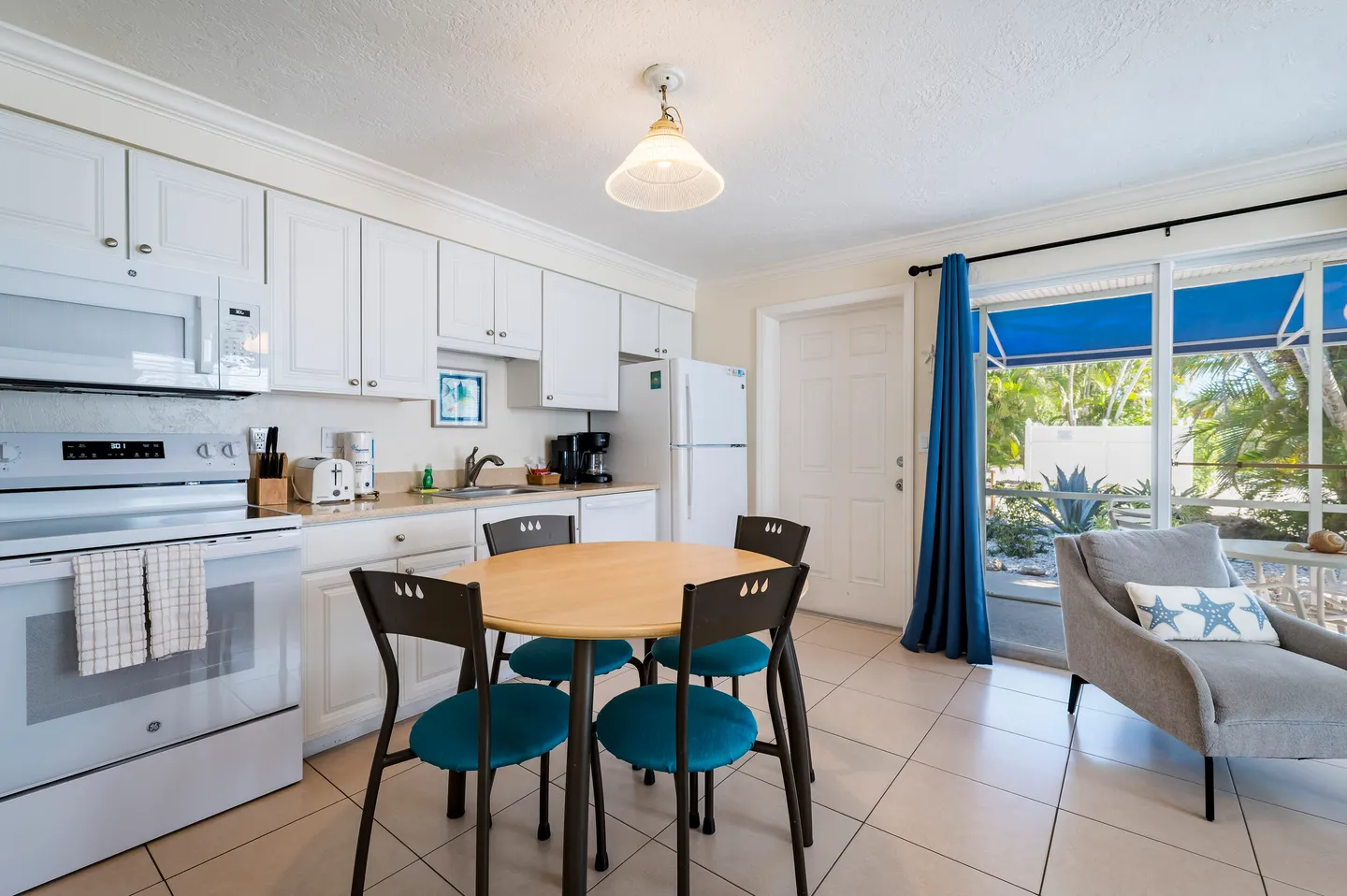 Open kitchen and dining area with white cabinets, round wooden table, and sliding glass doors leading outside.