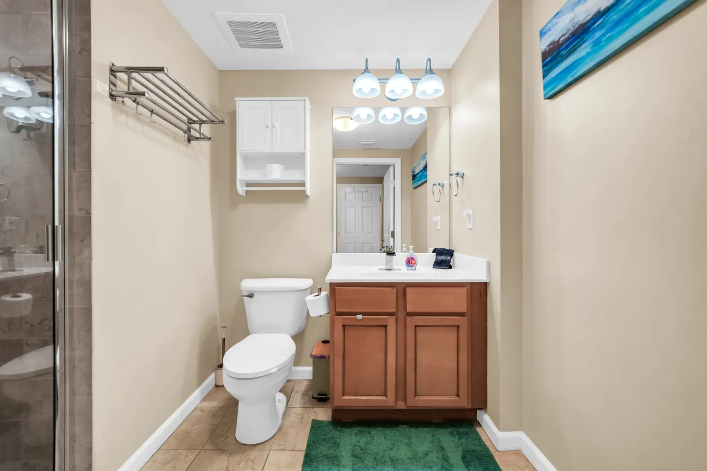 Bathroom featuring a wood vanity with a white countertop, toilet, mirror with overhead vanity lighting, and wall-mounted storage cabinet.