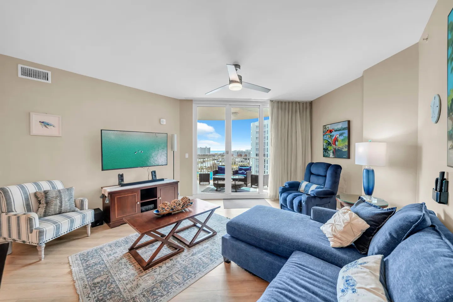 Living room featuring a blue sectional sofa, a coffee table, a mounted flat-screen TV, and sliding glass doors opening to a balcony.