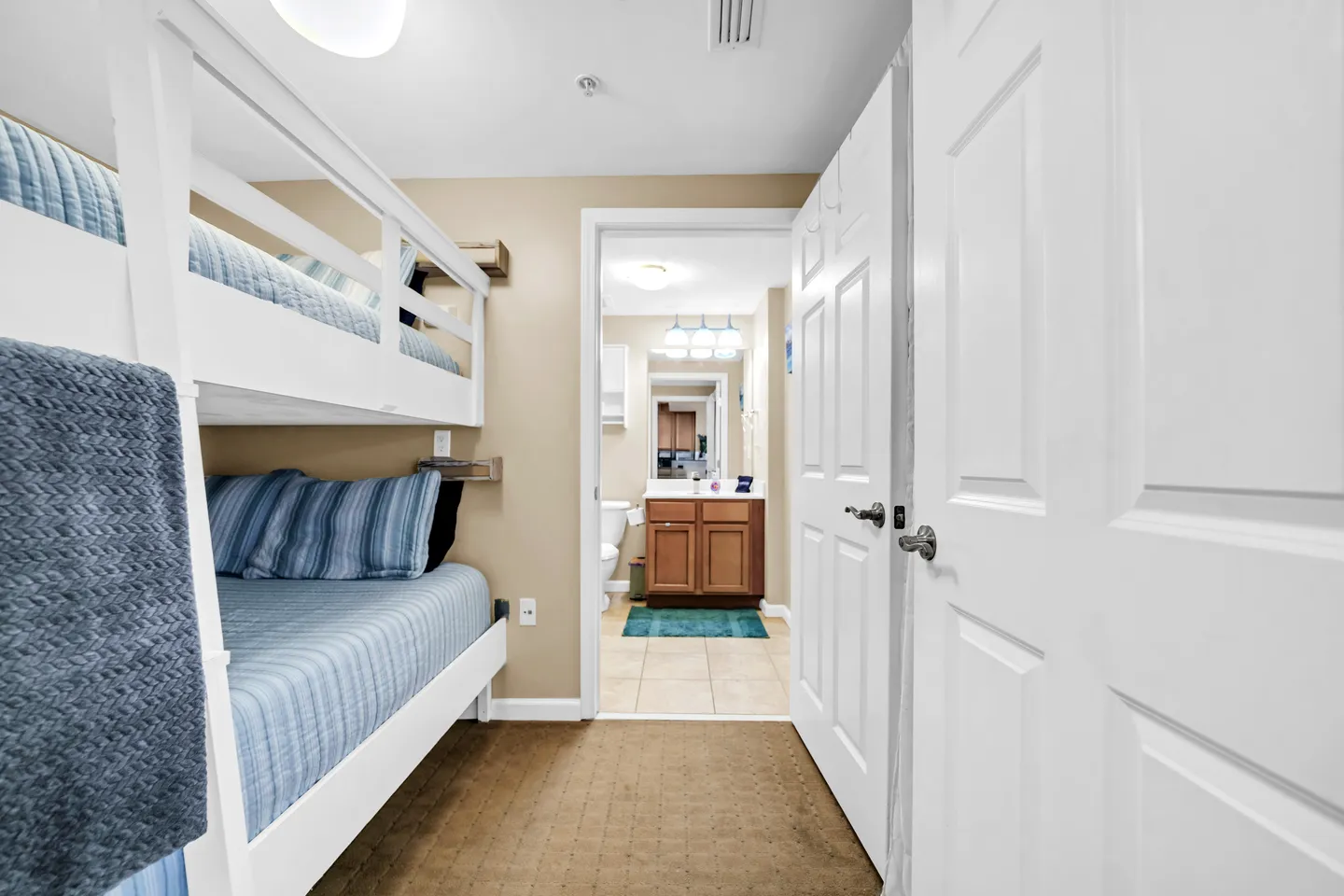 Bunk bed nook with white wooden frames and blue striped bedding leading into an ensuite bathroom.