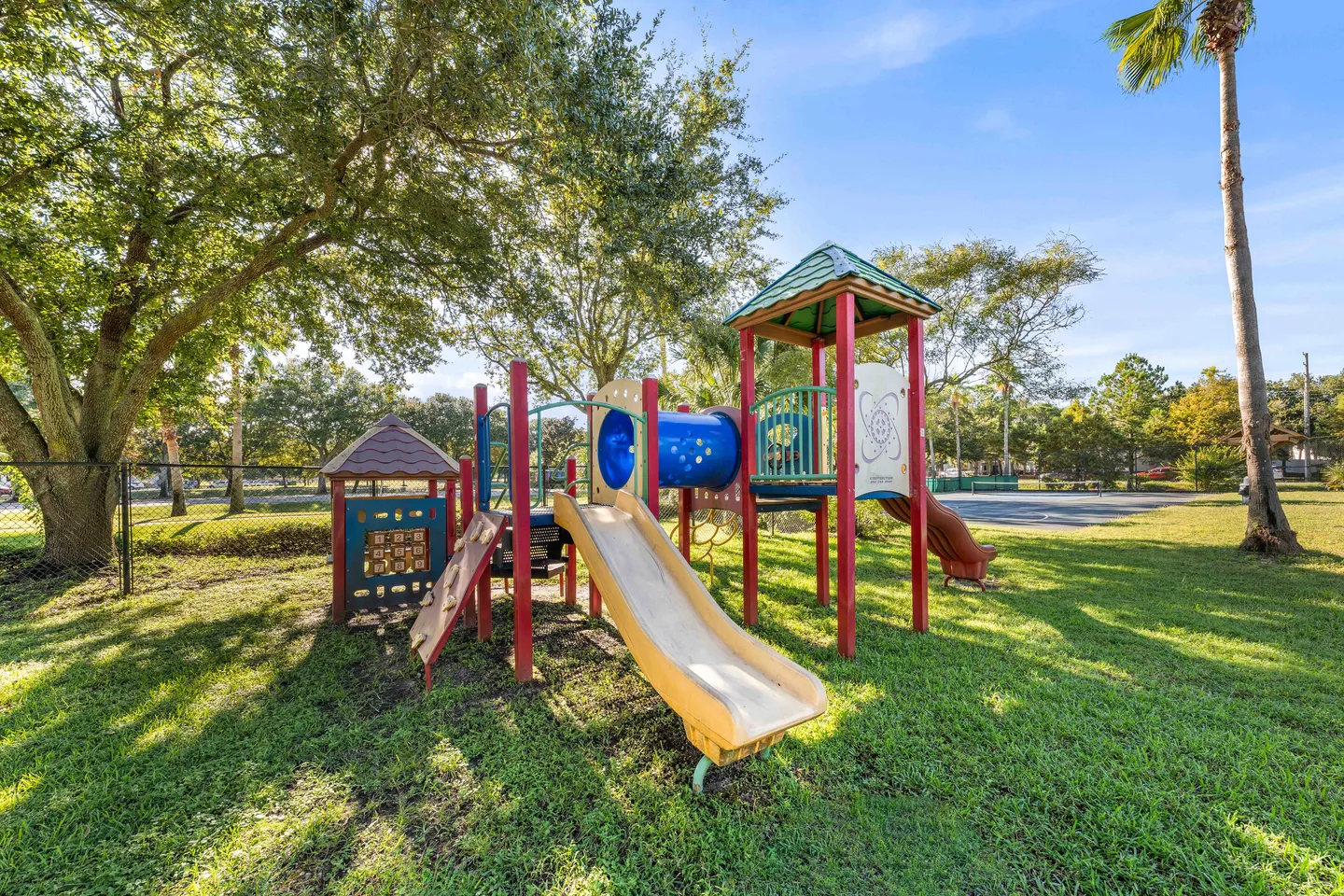 Outdoor community playground equipment with slides, climbing platforms, and a crawl tunnel on a grassy lawn.