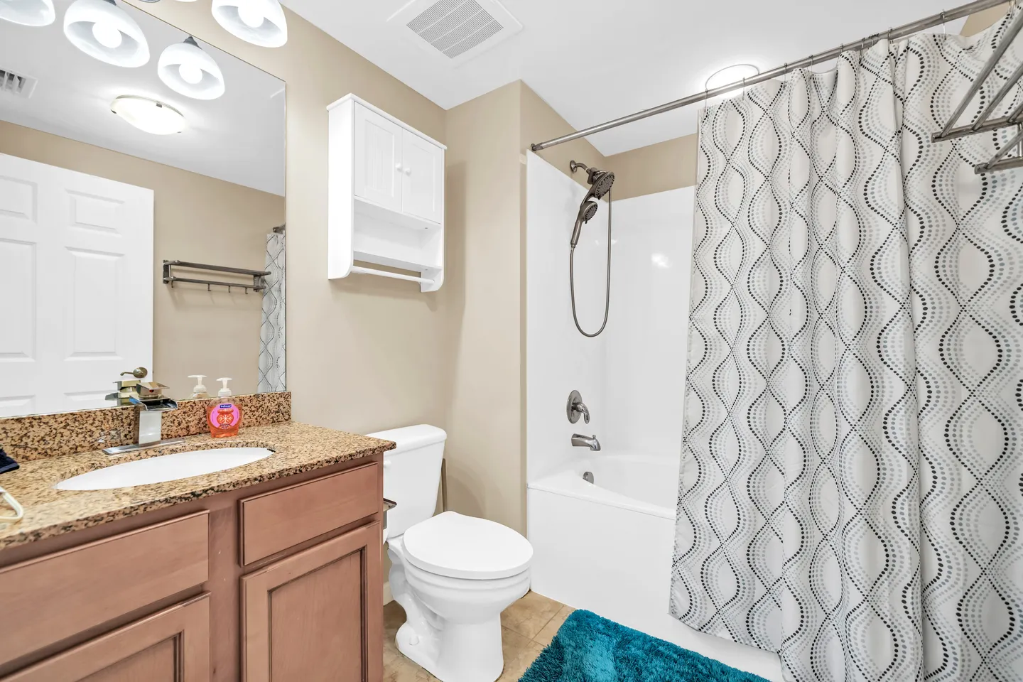 Bathroom featuring a vanity with speckled countertop, toilet, white medicine cabinet, and a shower-tub combination with a patterned curtain.
