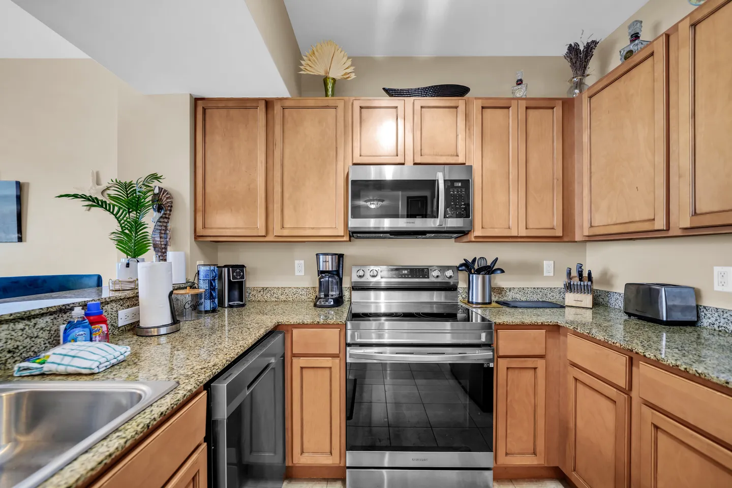 Kitchen corner with light wood cabinets, granite countertops, stainless steel electric range, microwave, and dishwasher.