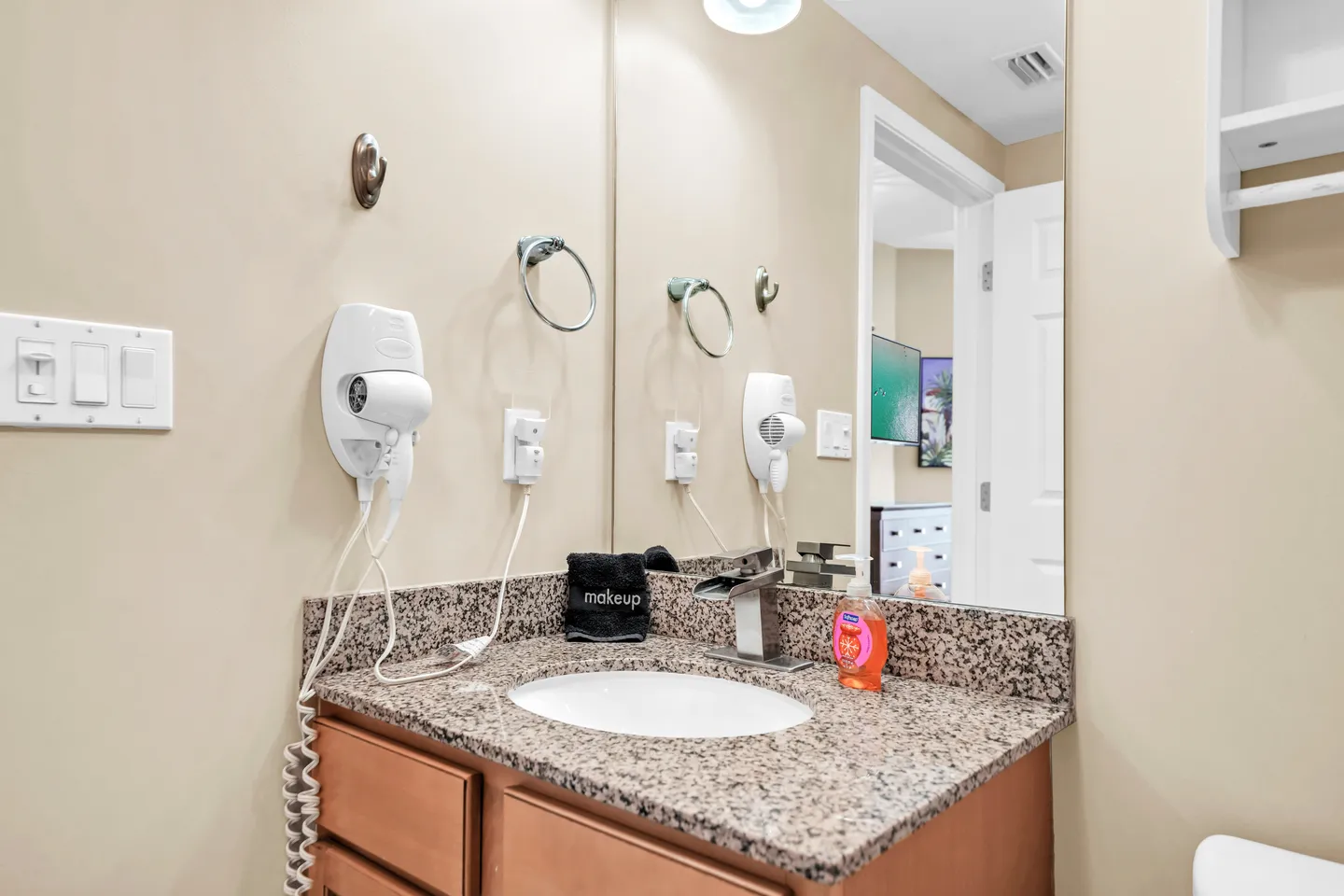 Bathroom vanity with a granite countertop, oval undermount sink, modern faucet, wall-mounted hair dryer, and large mirror.