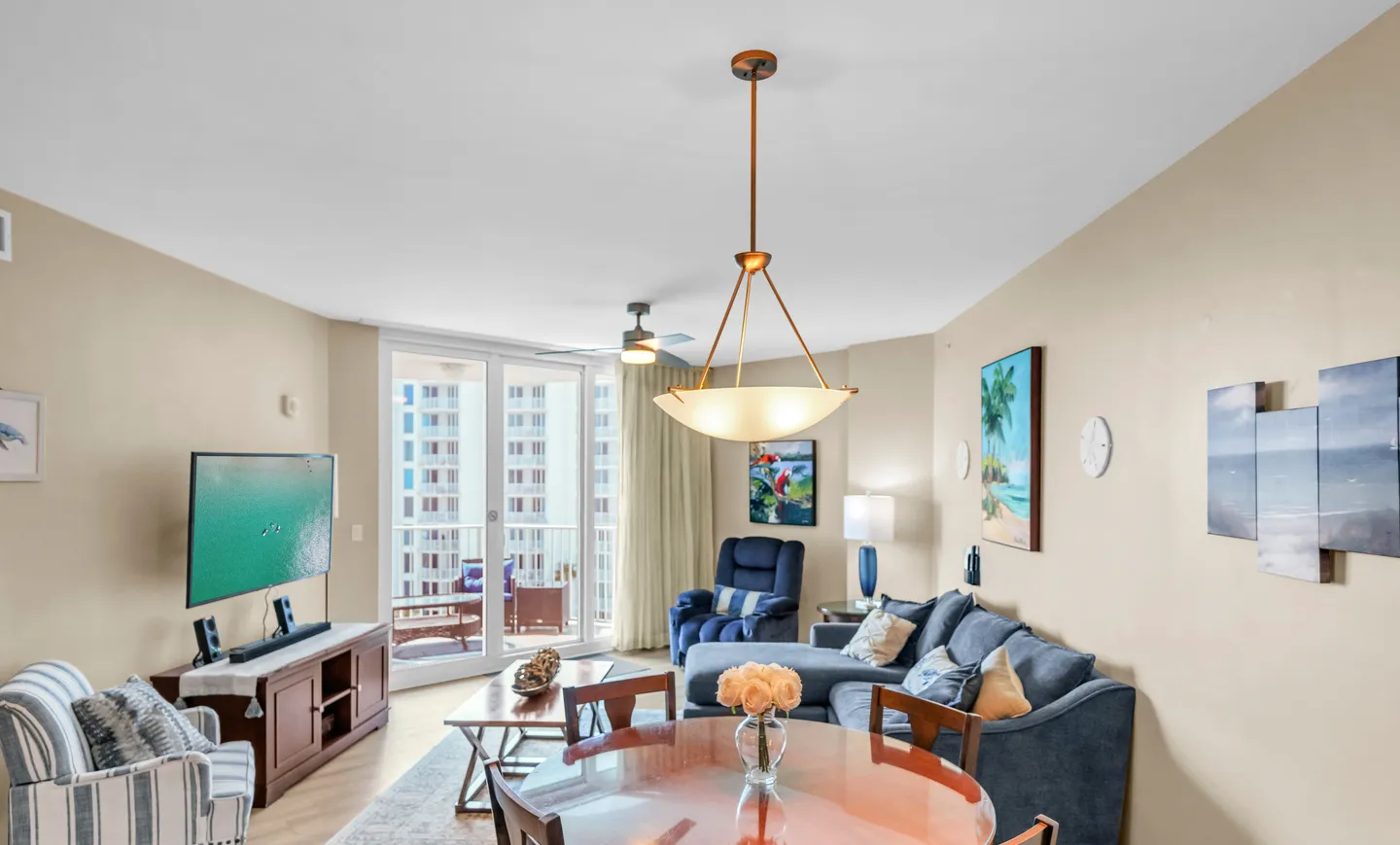Open living and dining area featuring a sectional sofa, television on a stand, dining table with chairs, and sliding glass doors to a balcony.