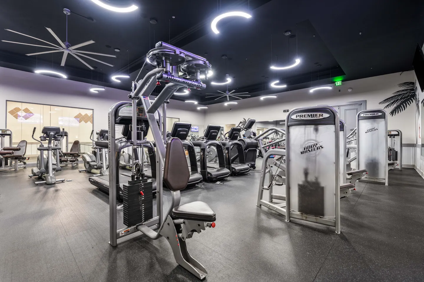 Indoor fitness center with various weight machines, treadmills, and contemporary curved ceiling lights.