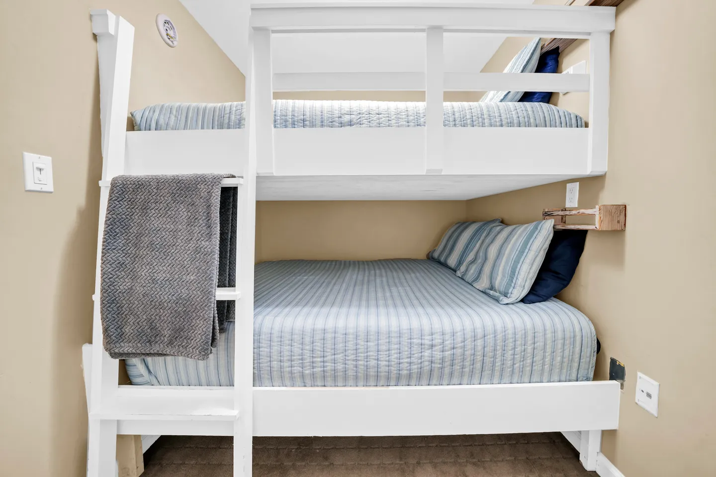 Built-in white wooden bunk bed with a ladder, blue striped bedding, and beige walls.