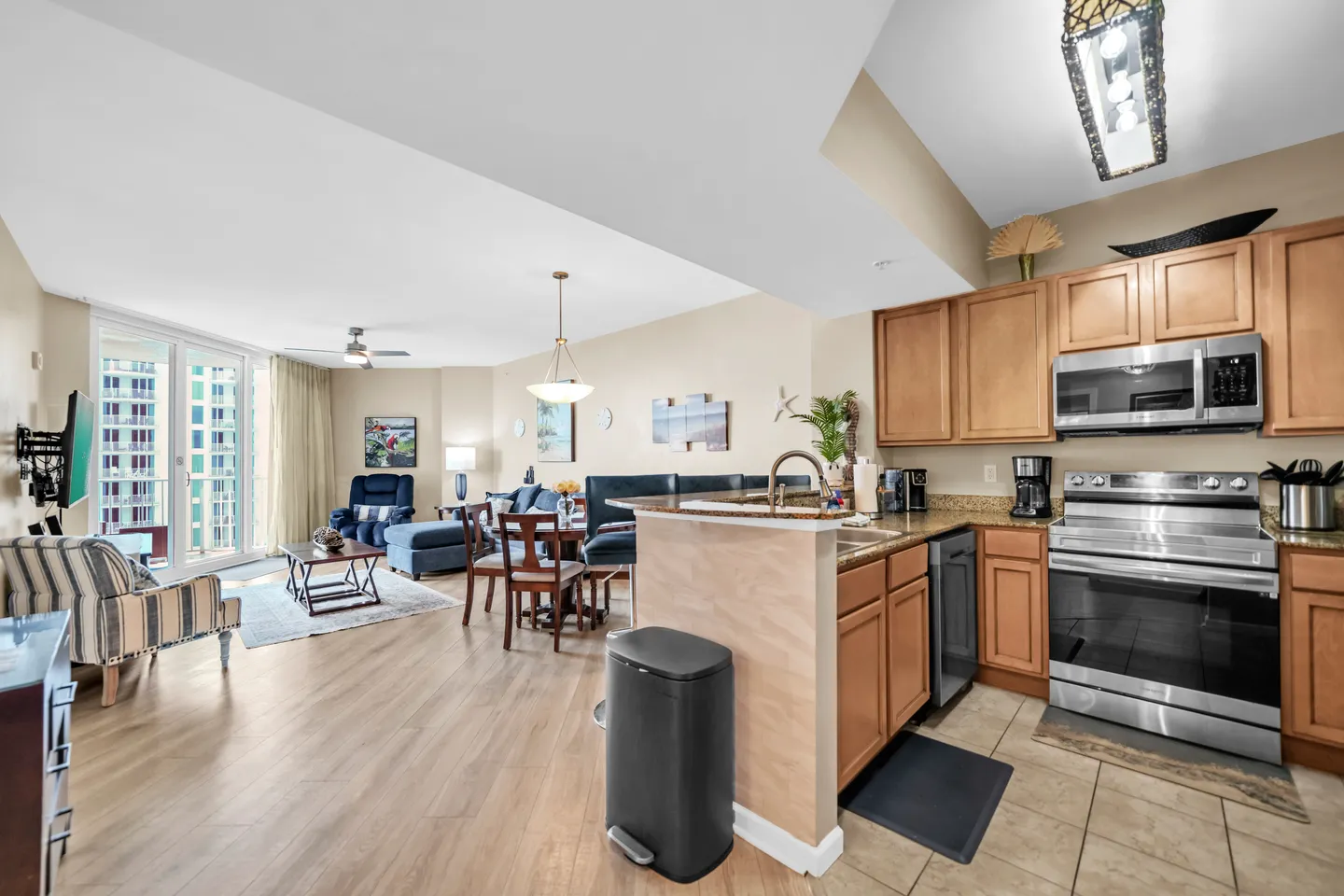 Open-concept condo interior featuring a kitchen with wood cabinets, dining table, and living room with sliding glass doors.