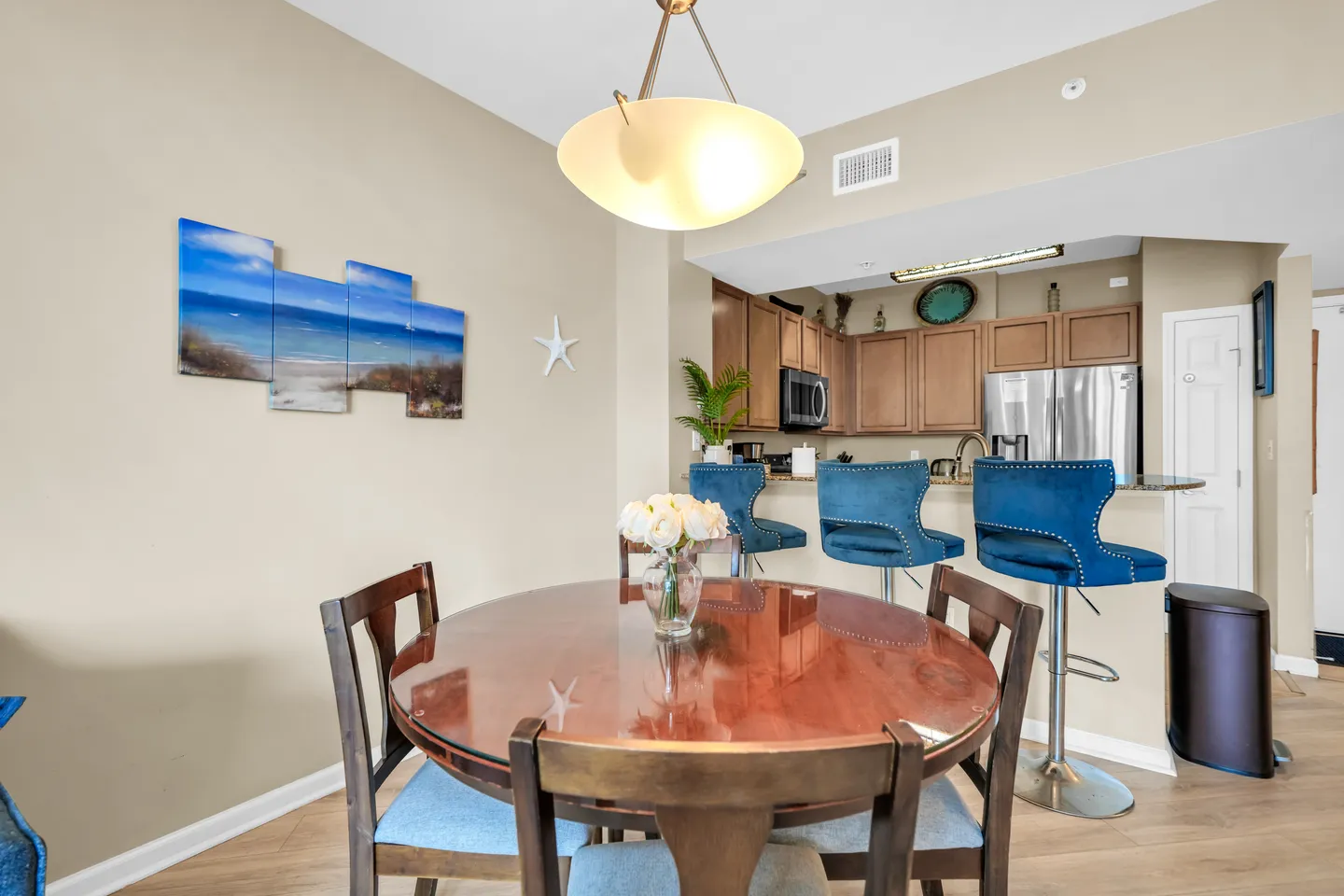 Dining area with a round wooden table and chairs, adjacent to a kitchen with blue barstools.