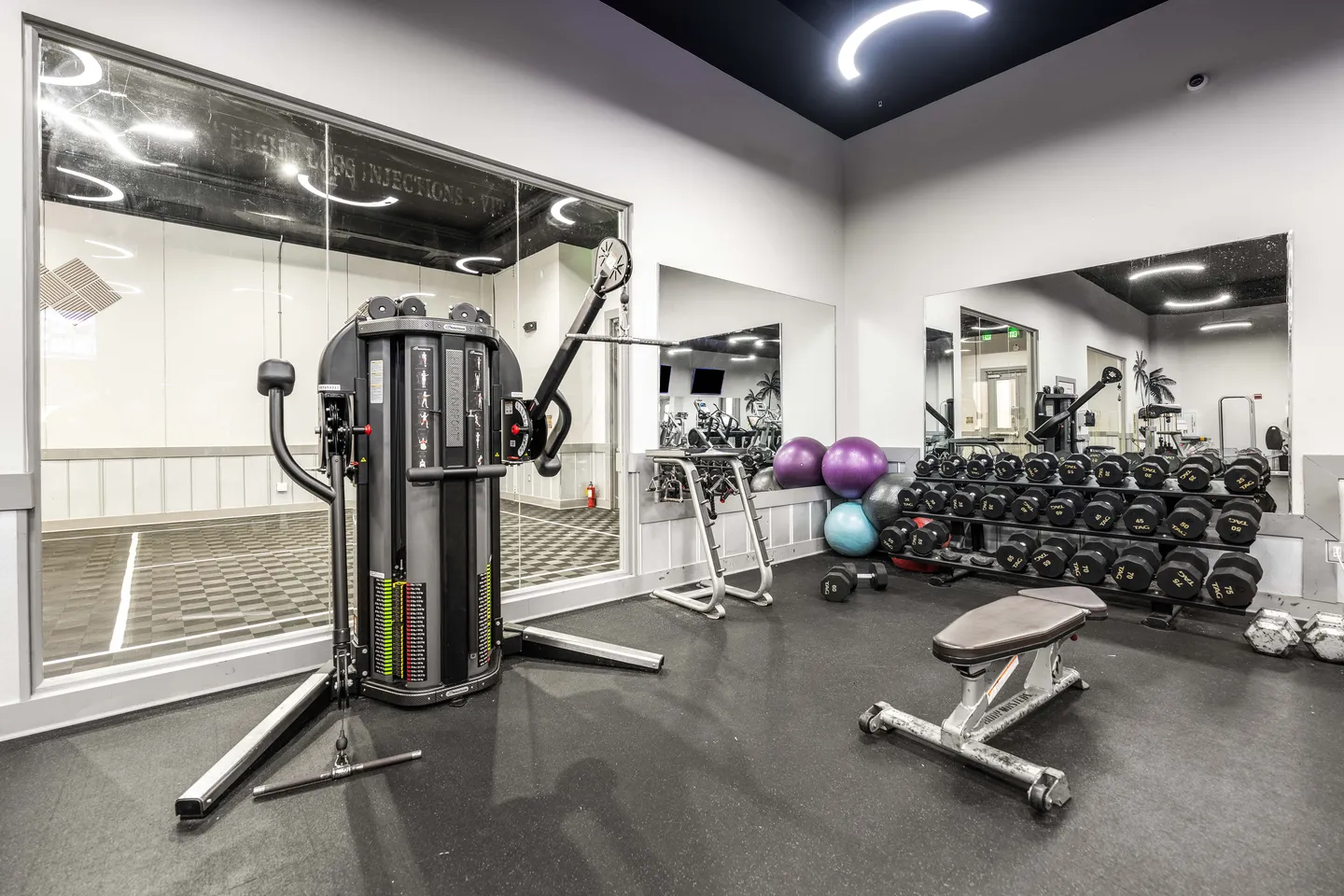 Fitness center with a multi-station cable machine, free weights on racks, a workout bench, and mirrored walls.