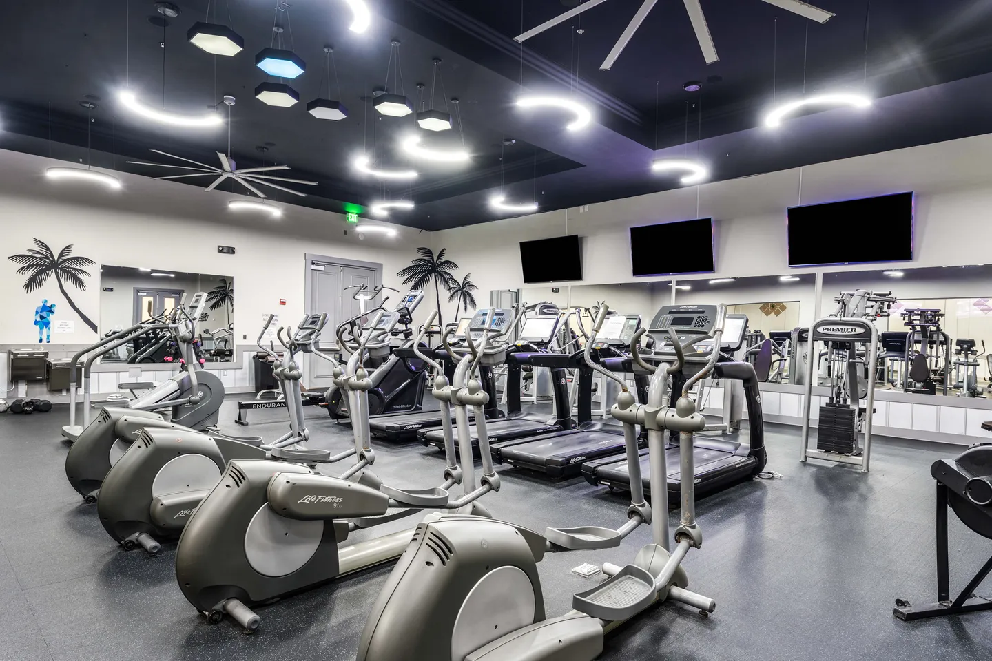 Commercial fitness center with rows of elliptical machines, treadmills, wall-mounted TVs, and large mirrors.