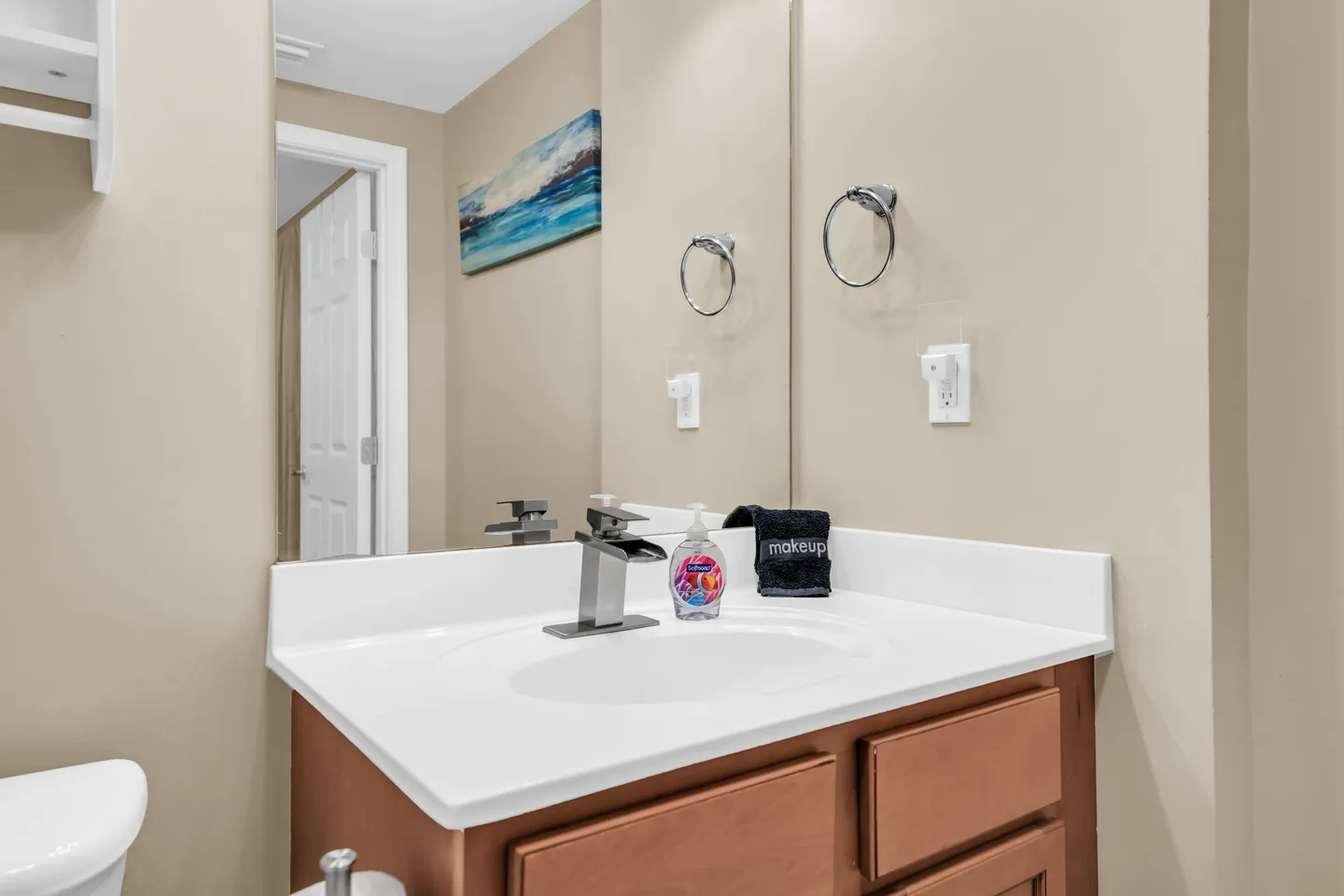 Bathroom vanity with a white countertop, modern dark faucet, and a large mirror reflecting an open doorway and wall art.