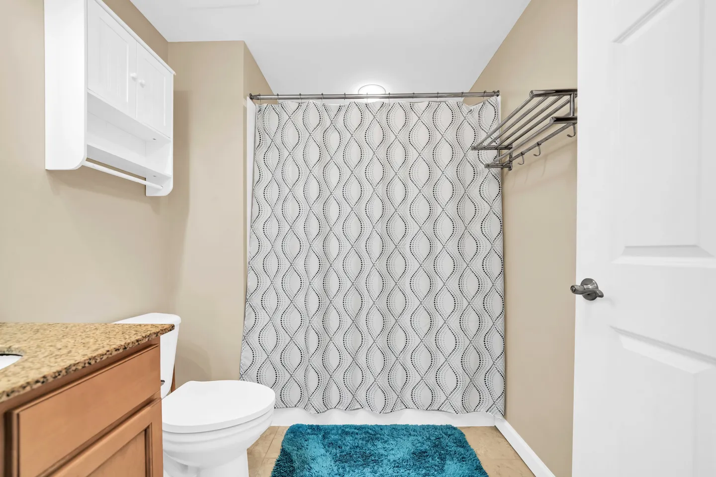 Bathroom showing a vanity counter, toilet, and a bathtub with a patterned shower curtain and blue bath mat.