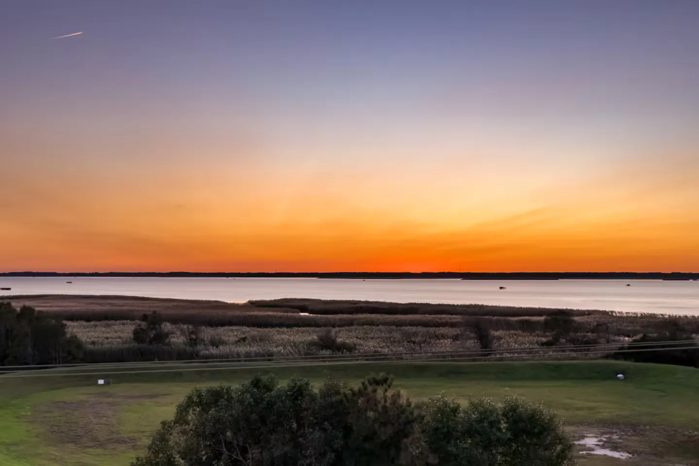 Scenic sunset view over a wide body of water and wetland marsh from an elevated vantage point.