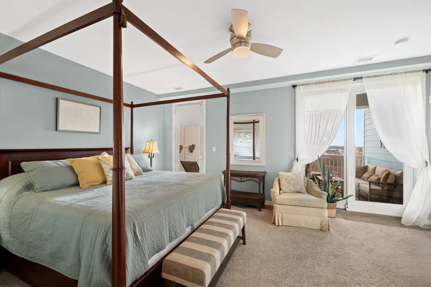 Bedroom with a wooden canopy bed, bench, armchair, and sliding glass doors leading to a balcony.