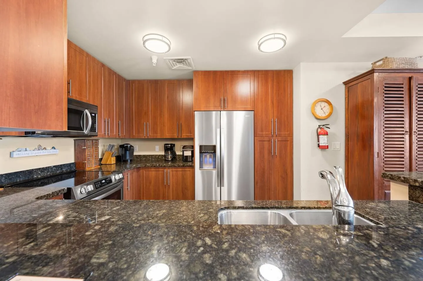 Kitchen with dark polished countertops, wood cabinets, stainless steel refrigerator, and double sink.