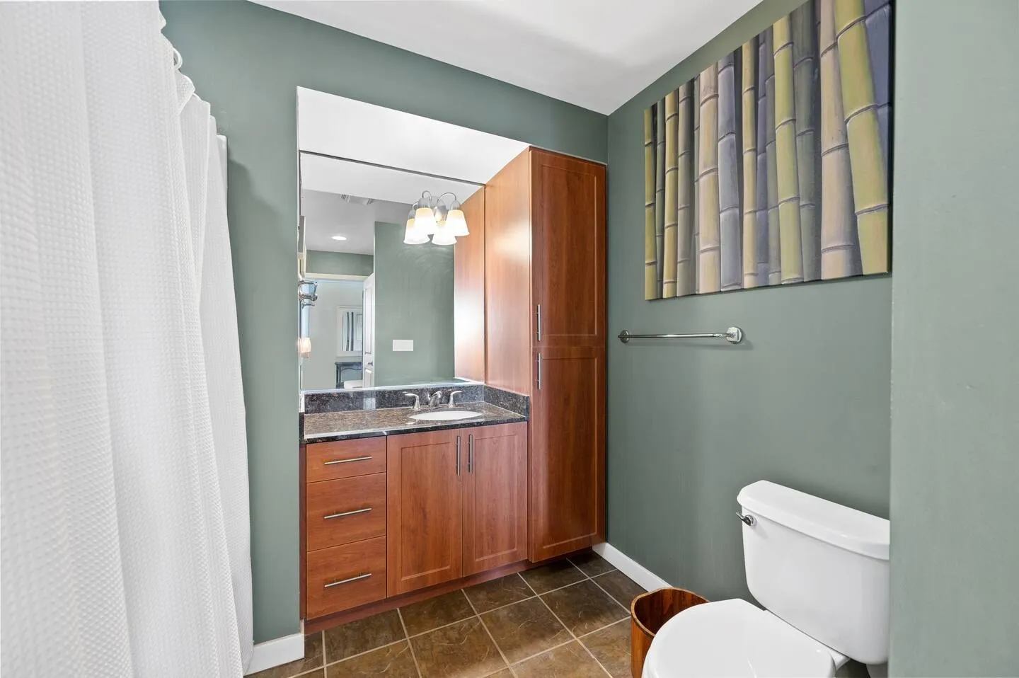 Bathroom featuring a dark wood vanity with dark countertop, large mirror, tall cabinet, toilet, and green walls with bamboo art.
