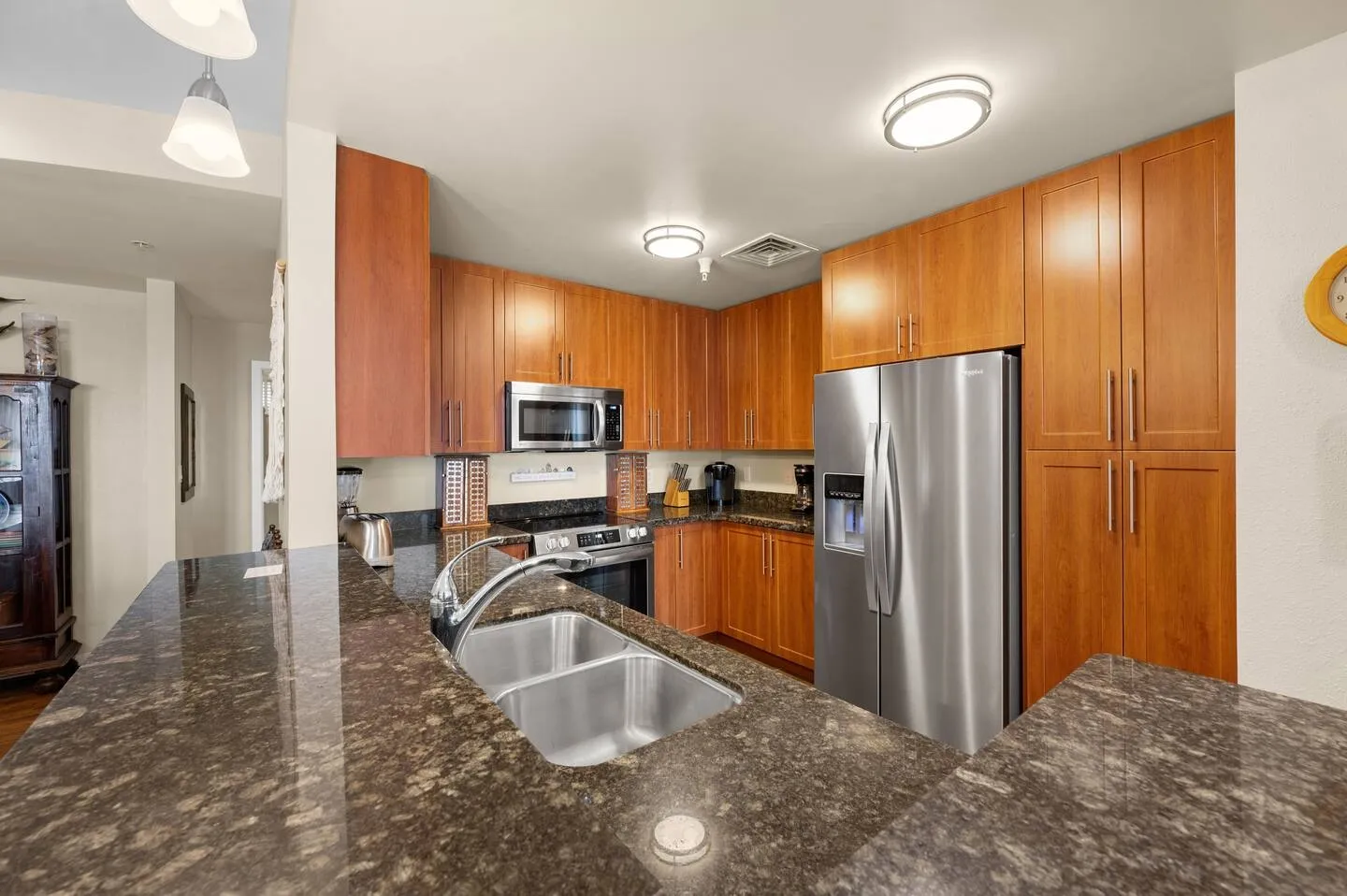 Kitchen with warm wood cabinetry, dark granite-style countertops, double sink, and stainless steel refrigerator.