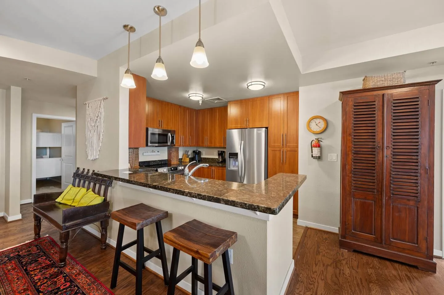 Open kitchen featuring a breakfast bar with two wooden stools, stainless steel appliances, and wood cabinetry.