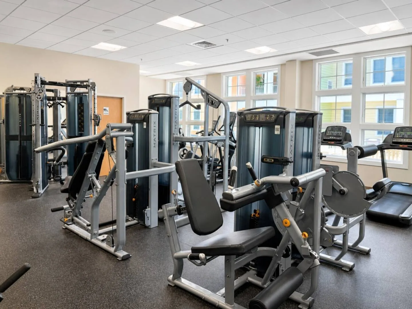 Indoor fitness center featuring Matrix weight machines and cardio equipment next to large windows.