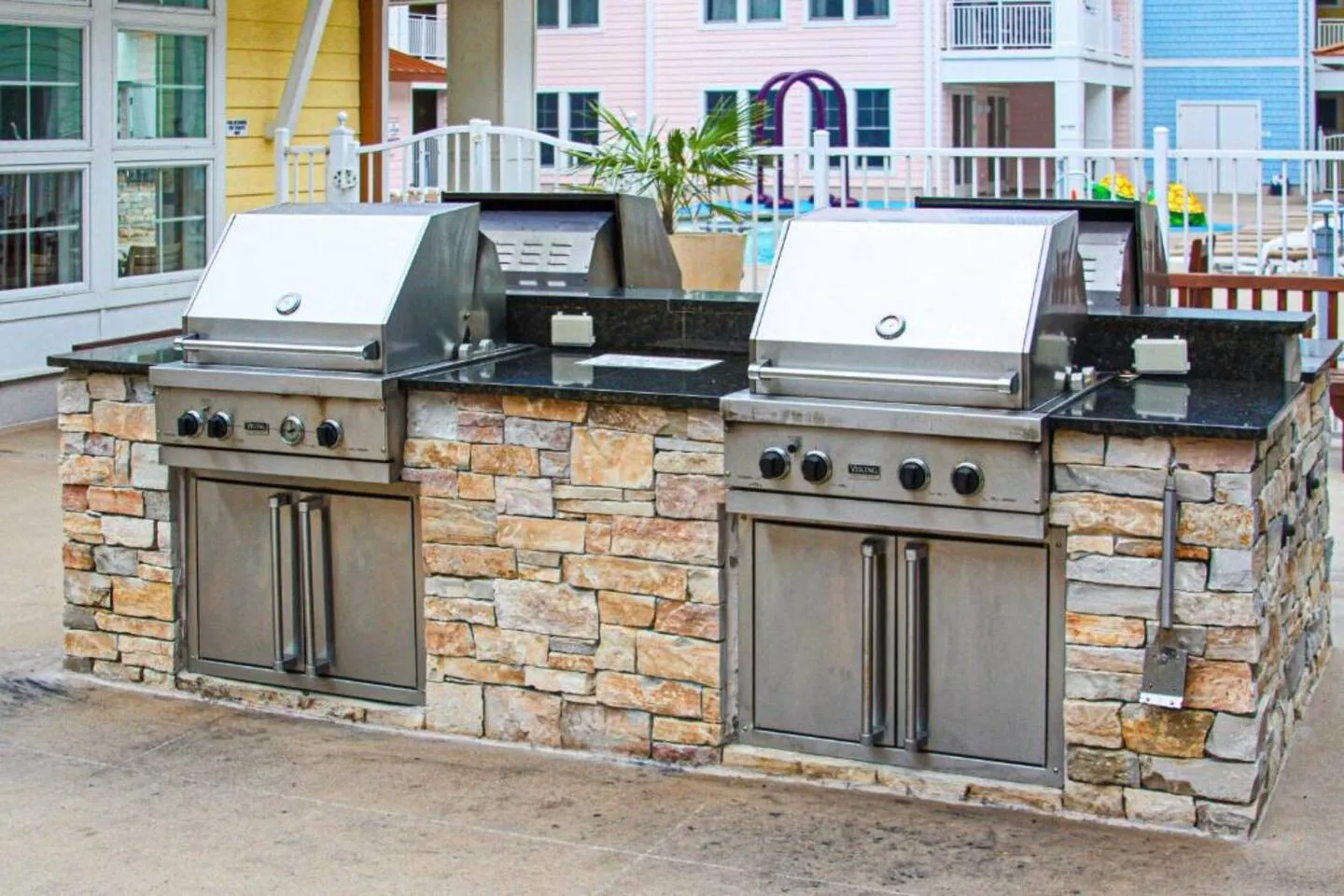 Outdoor grilling station with stainless steel grills built into a stone and black countertop island.