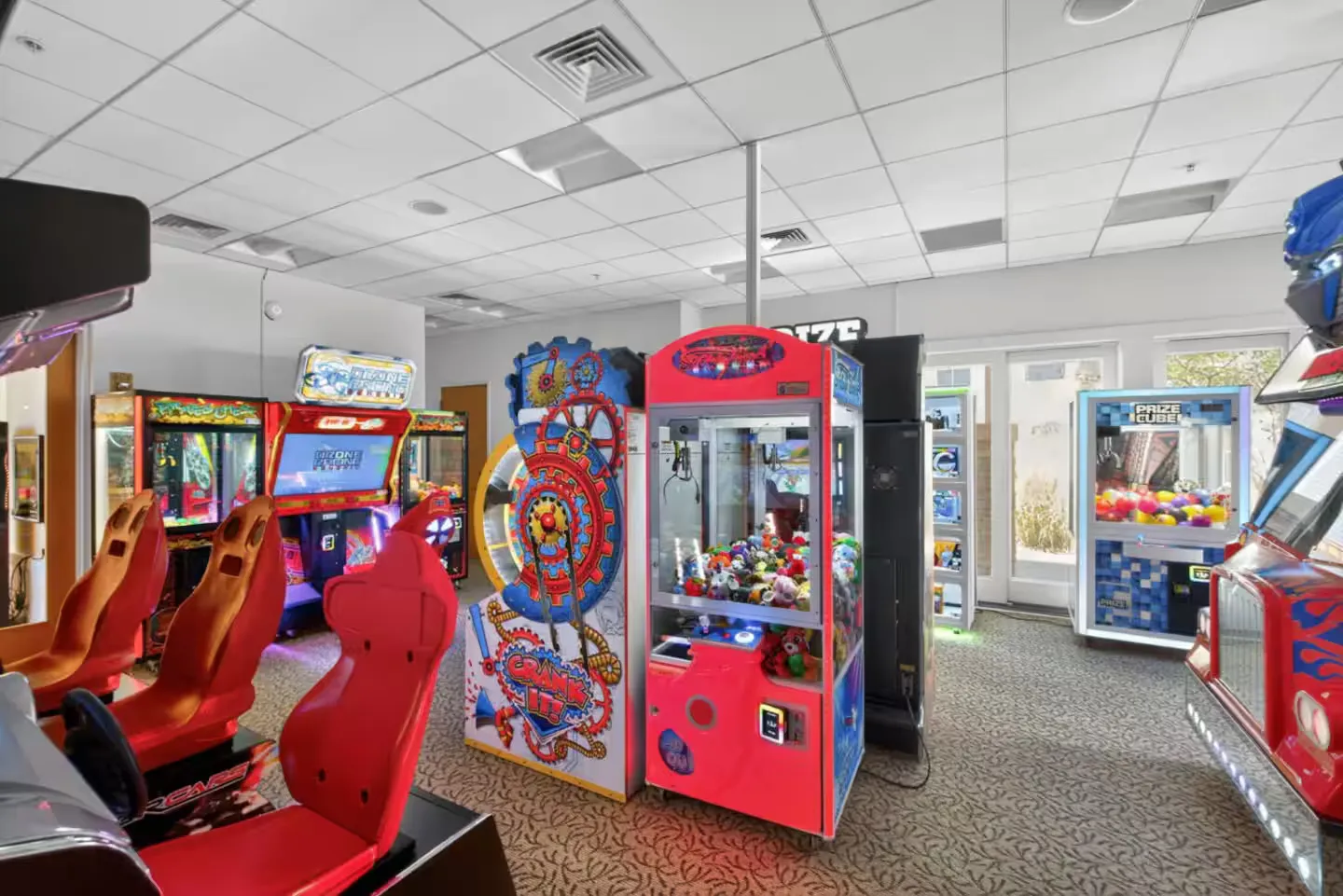 Arcade game room with various claw machines, driving simulators with red bucket seats, and prize games.