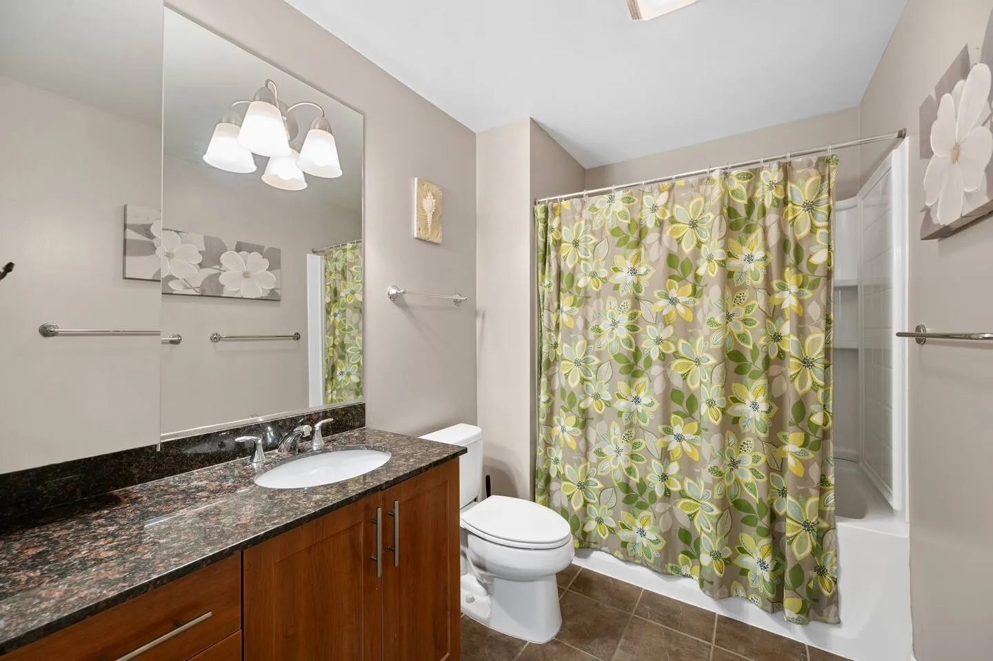 Bathroom with a dark granite-topped wooden vanity, toilet, and floral shower curtain over a shower-tub combination.