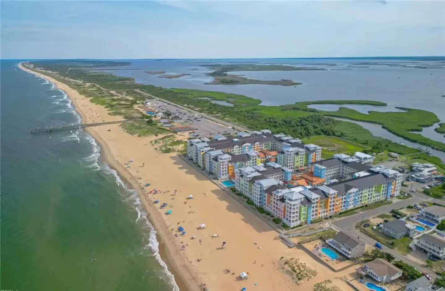 Aerial view of a colorful beachfront resort complex situated along a sandy beach and ocean on a narrow peninsula.