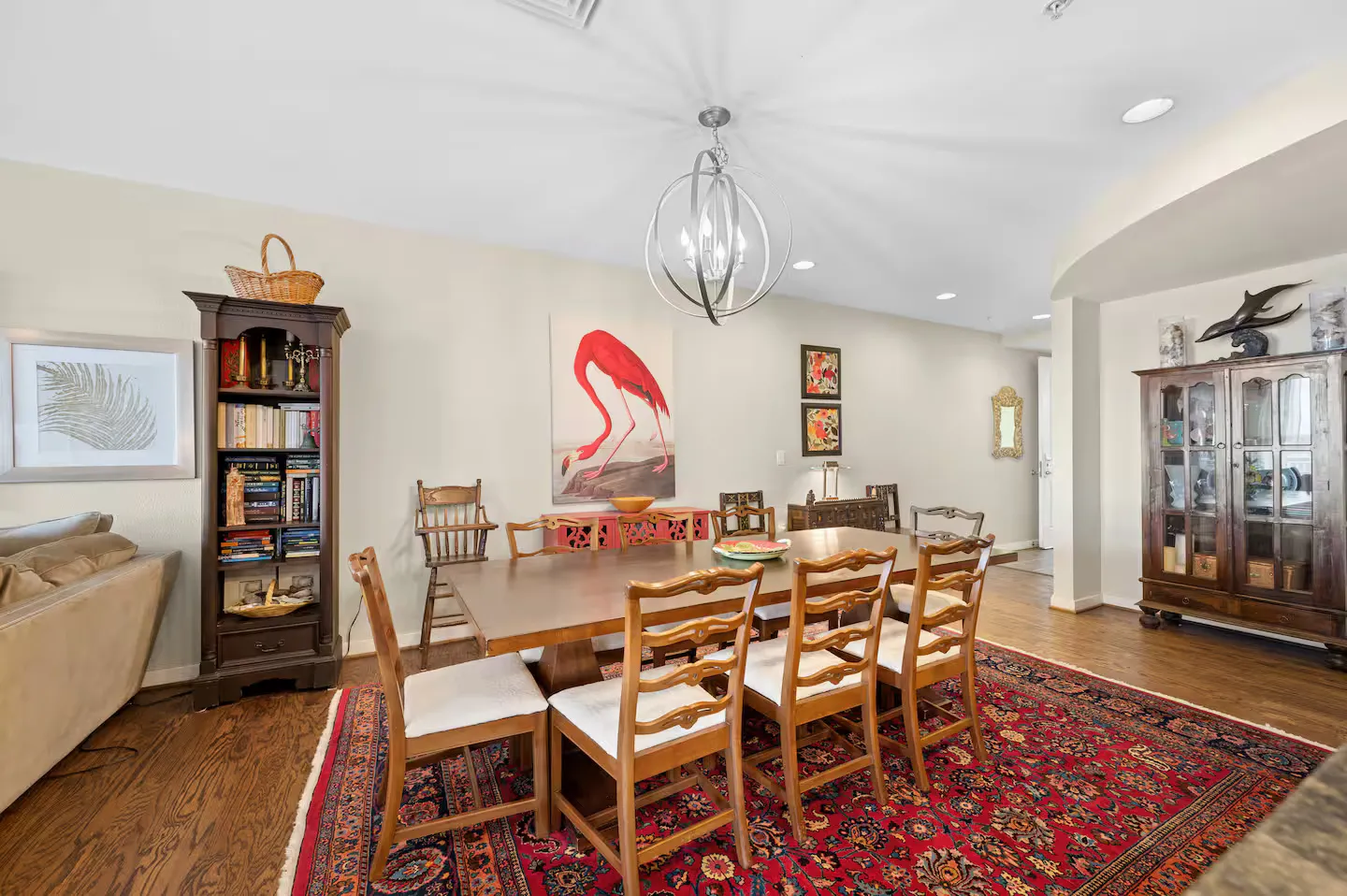 Dining area featuring a wooden dining table with chairs over a patterned red rug, illuminated by a spherical chandelier.