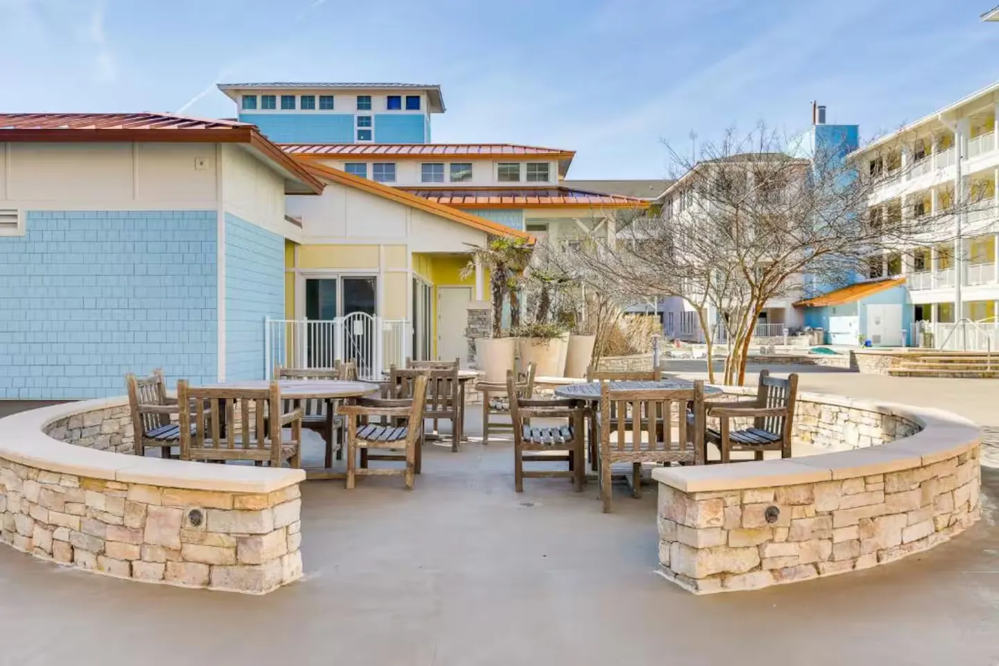 Outdoor courtyard patio featuring wooden dining tables and chairs partially enclosed by a low stone wall.