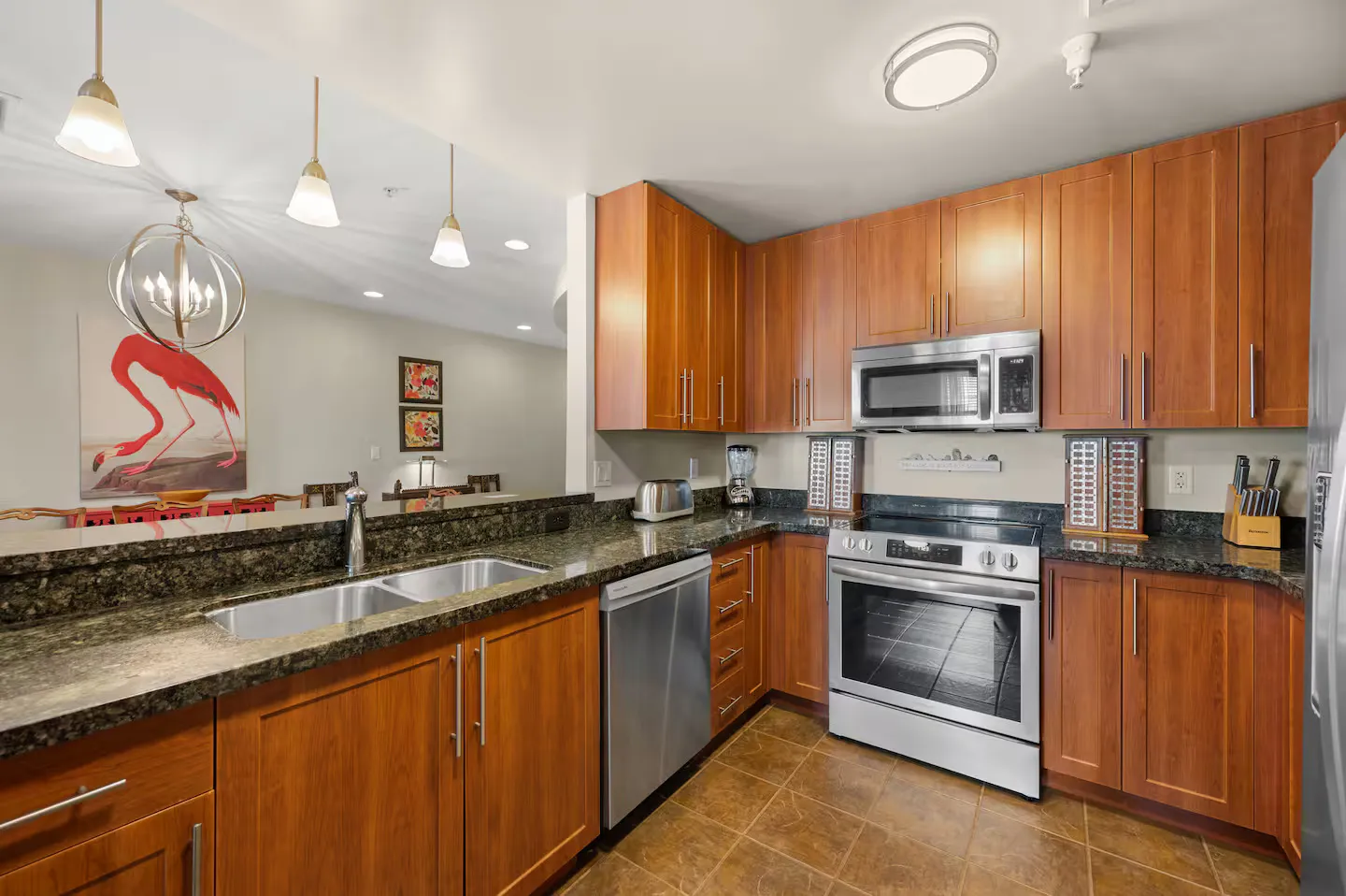 Kitchen with warm wood cabinetry, dark granite countertops, stainless steel appliances, and a pass-through counter looking into the dining area.