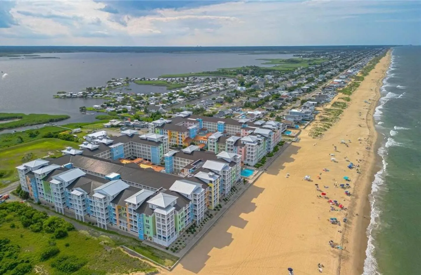 Aerial view of a colorful oceanfront condominium complex along a sandy beach and coastline.