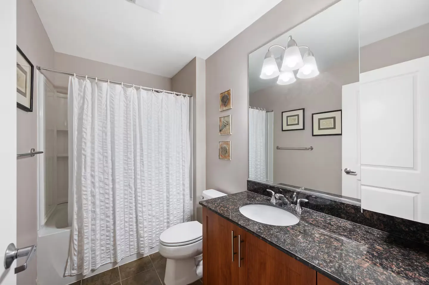 Bathroom with a vanity, large mirror, toilet, and shower-tub combination with a white curtain.
