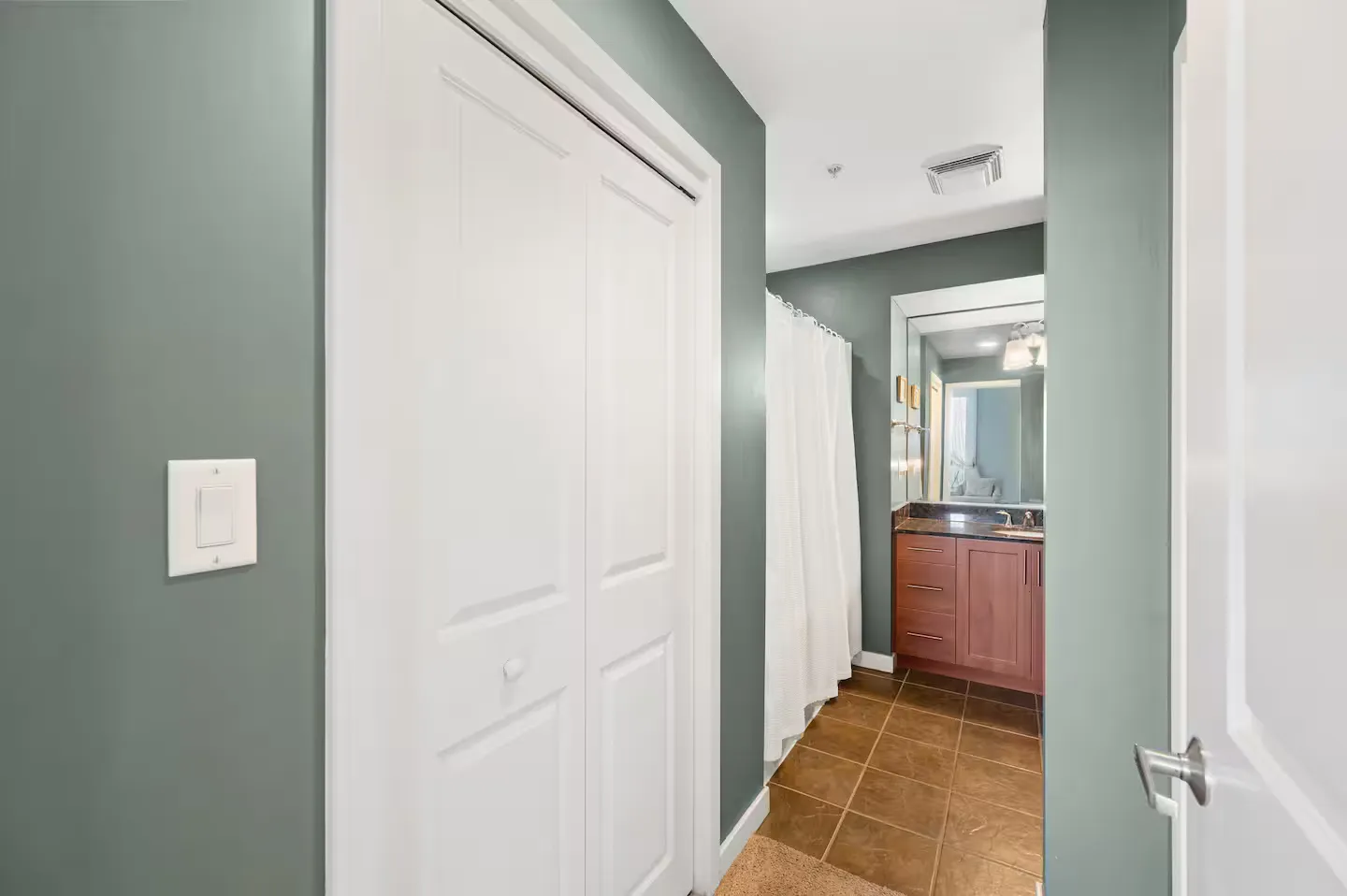 Hallway entrance leading into a bathroom with tile flooring, vanity, and a shower curtain.