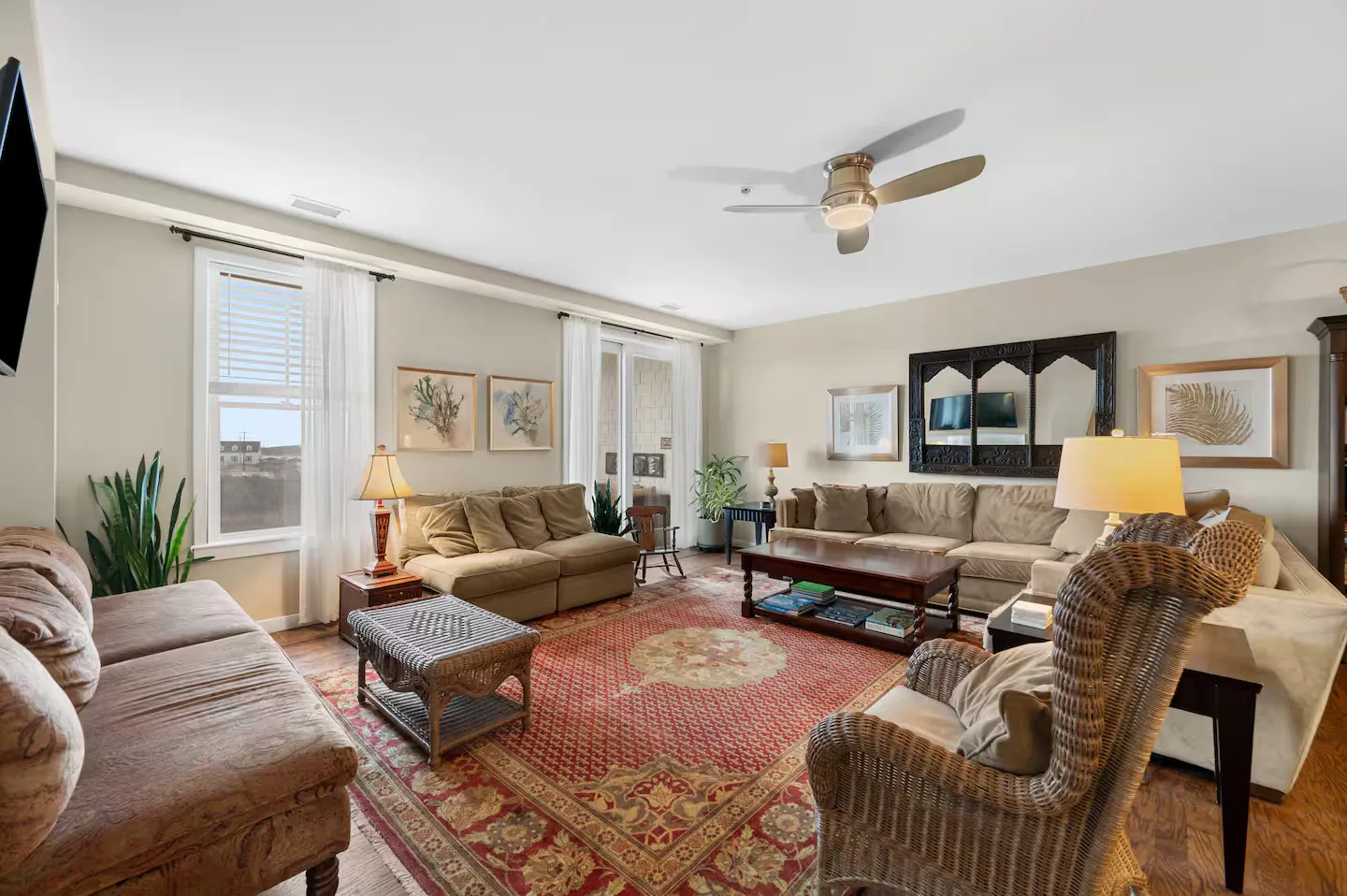 Spacious living room featuring multiple couches, a wicker armchair, coffee tables, an ornate area rug, and a ceiling fan.