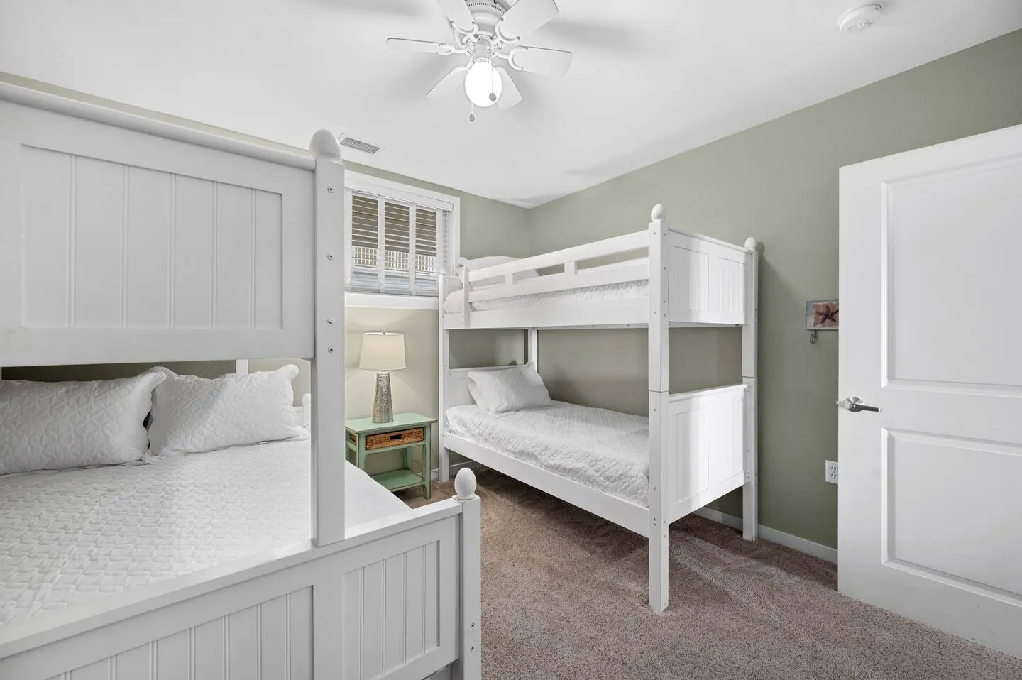Bedroom with two sets of white painted wooden bunk beds, carpeted floor, ceiling fan, and light green walls.