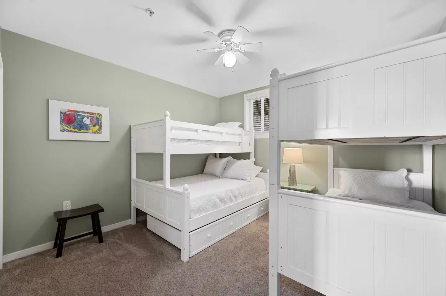 Bedroom with two white bunk bed sets, carpeted floor, light green accent wall, and a ceiling fan.