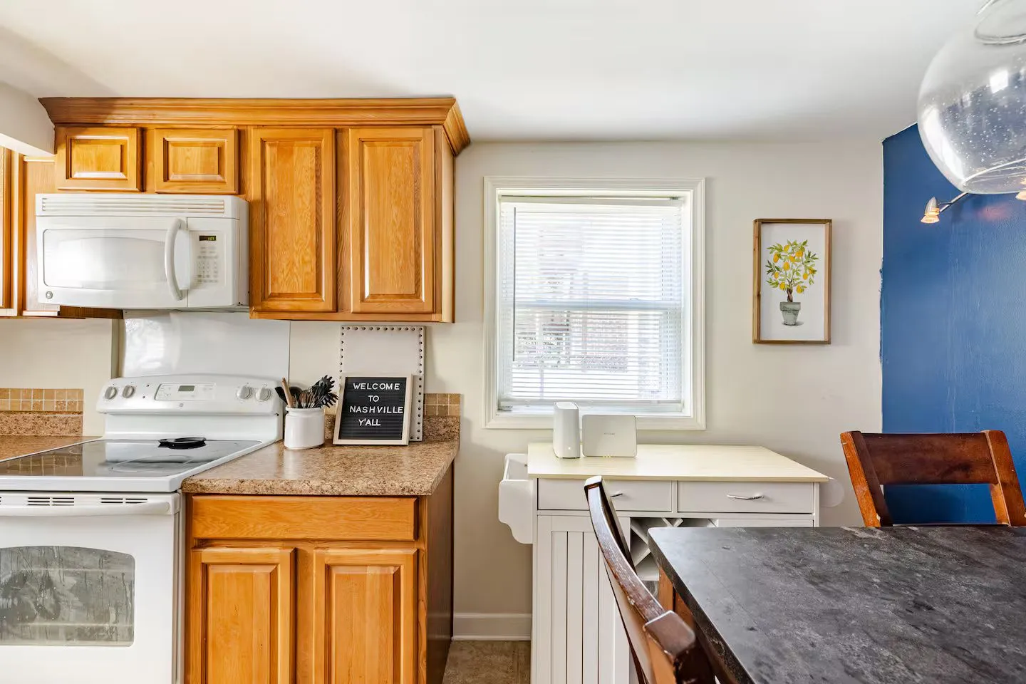 Kitchen and dining area featuring wood cabinetry, white appliances, a window with blinds, and a dining table with chairs.