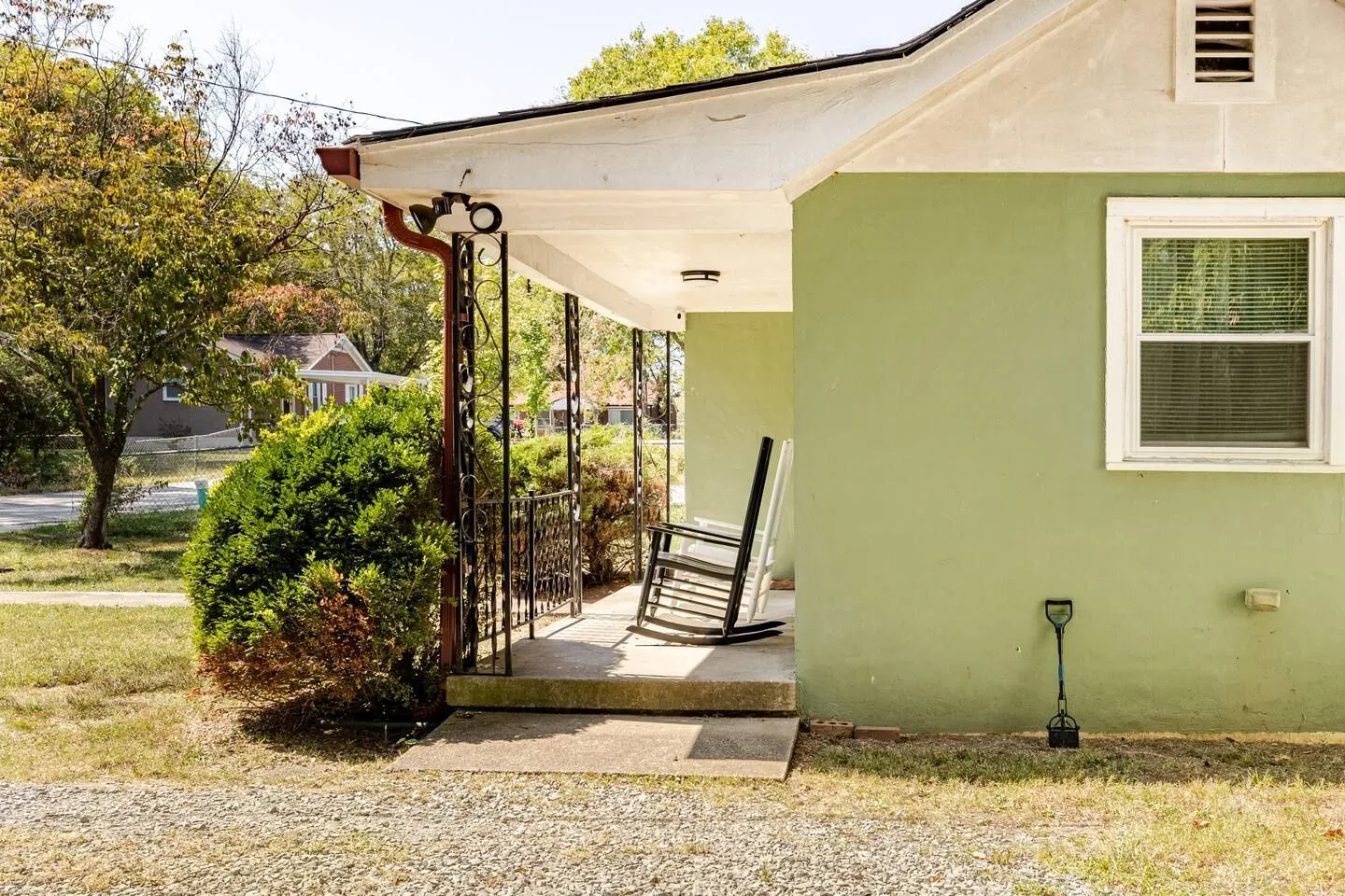 Front porch of a light green house with rocking chairs and decorative metal railings.