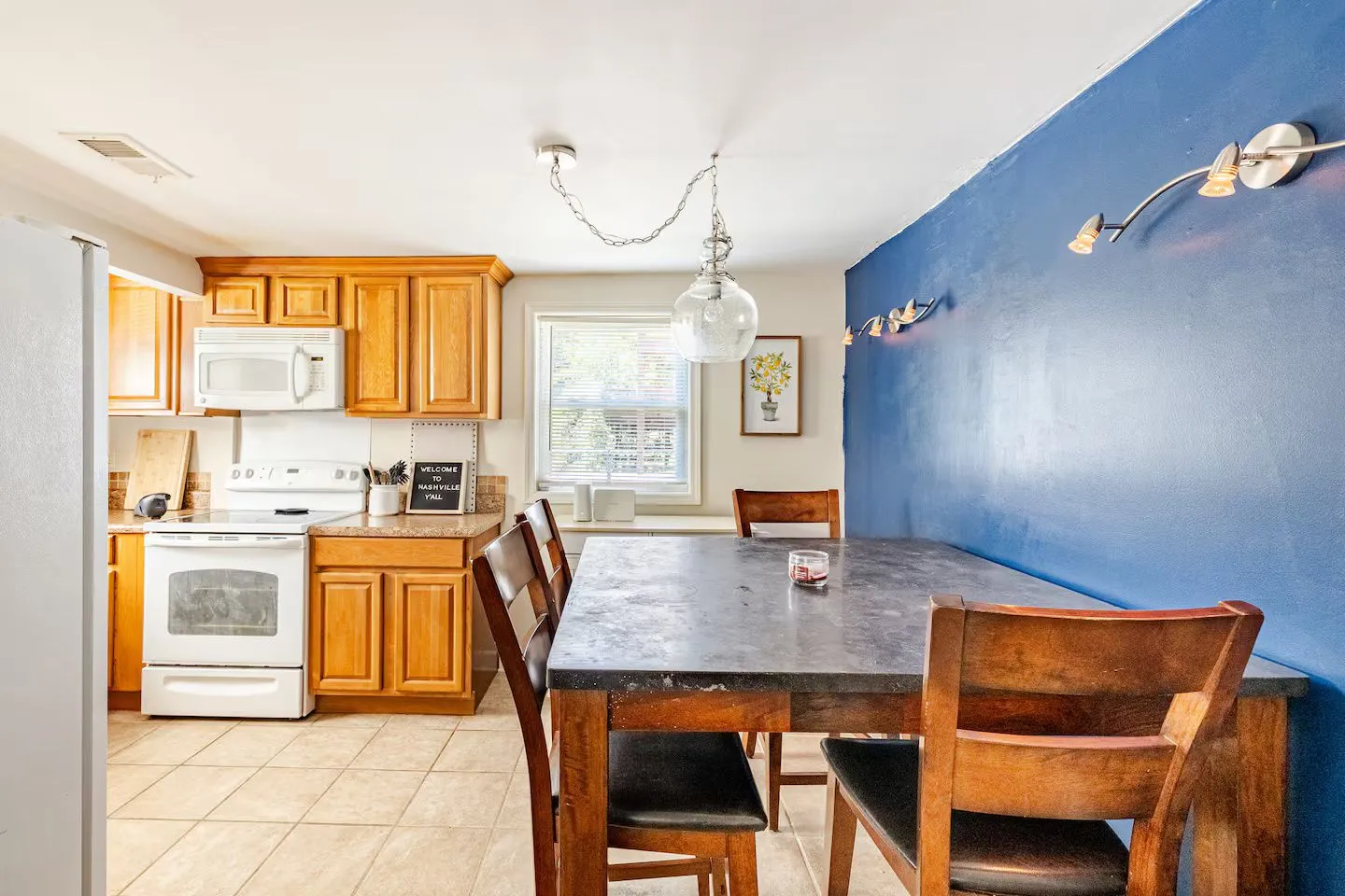 Dining area with a wooden table and chairs adjacent to a kitchen with light wood cabinets and white appliances.