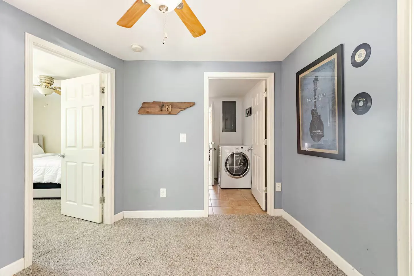 Hallway with light blue walls and carpet leading to an open laundry room and a bedroom.