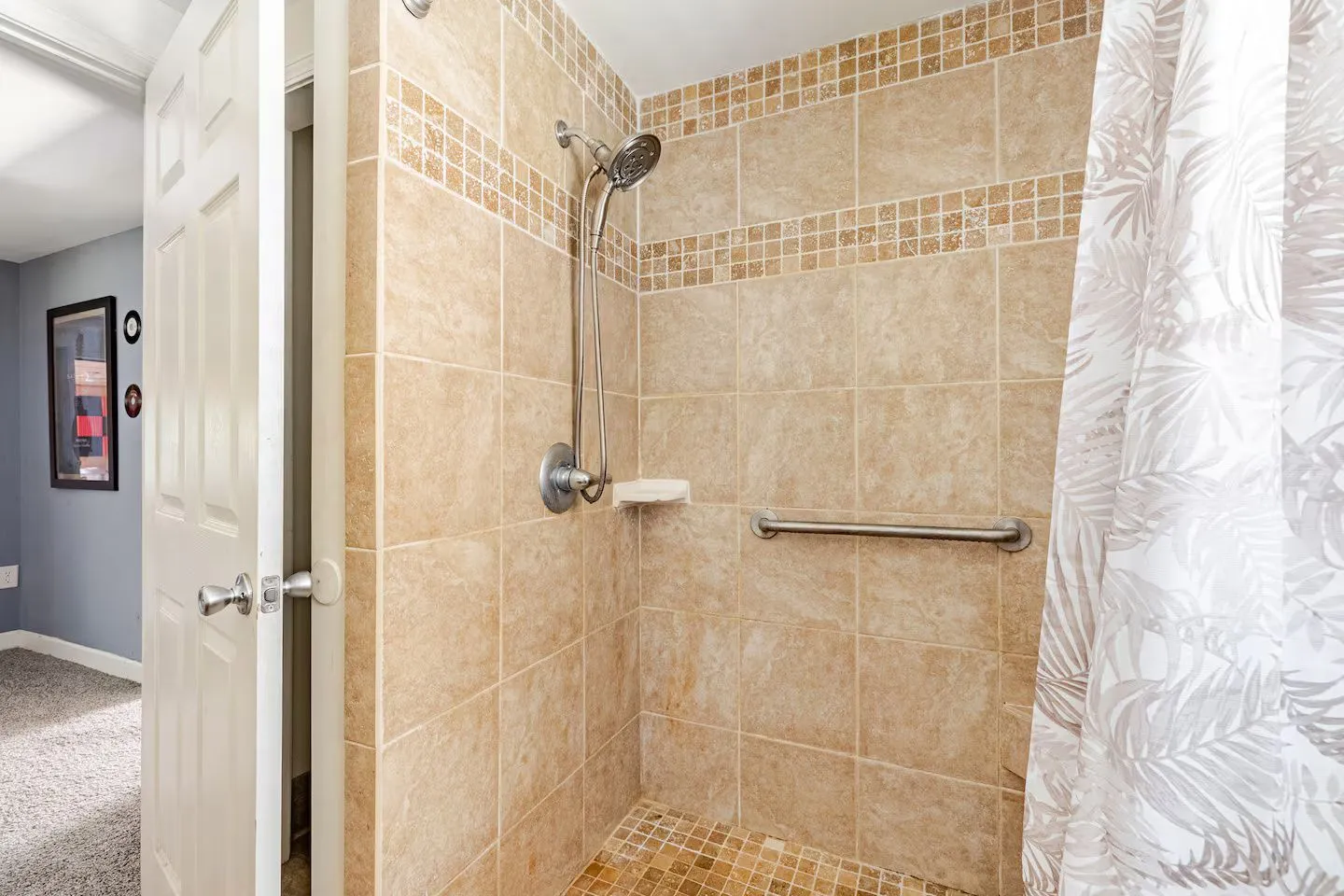 Tiled walk-in shower with handheld showerhead, grab bar, and patterned shower curtain
